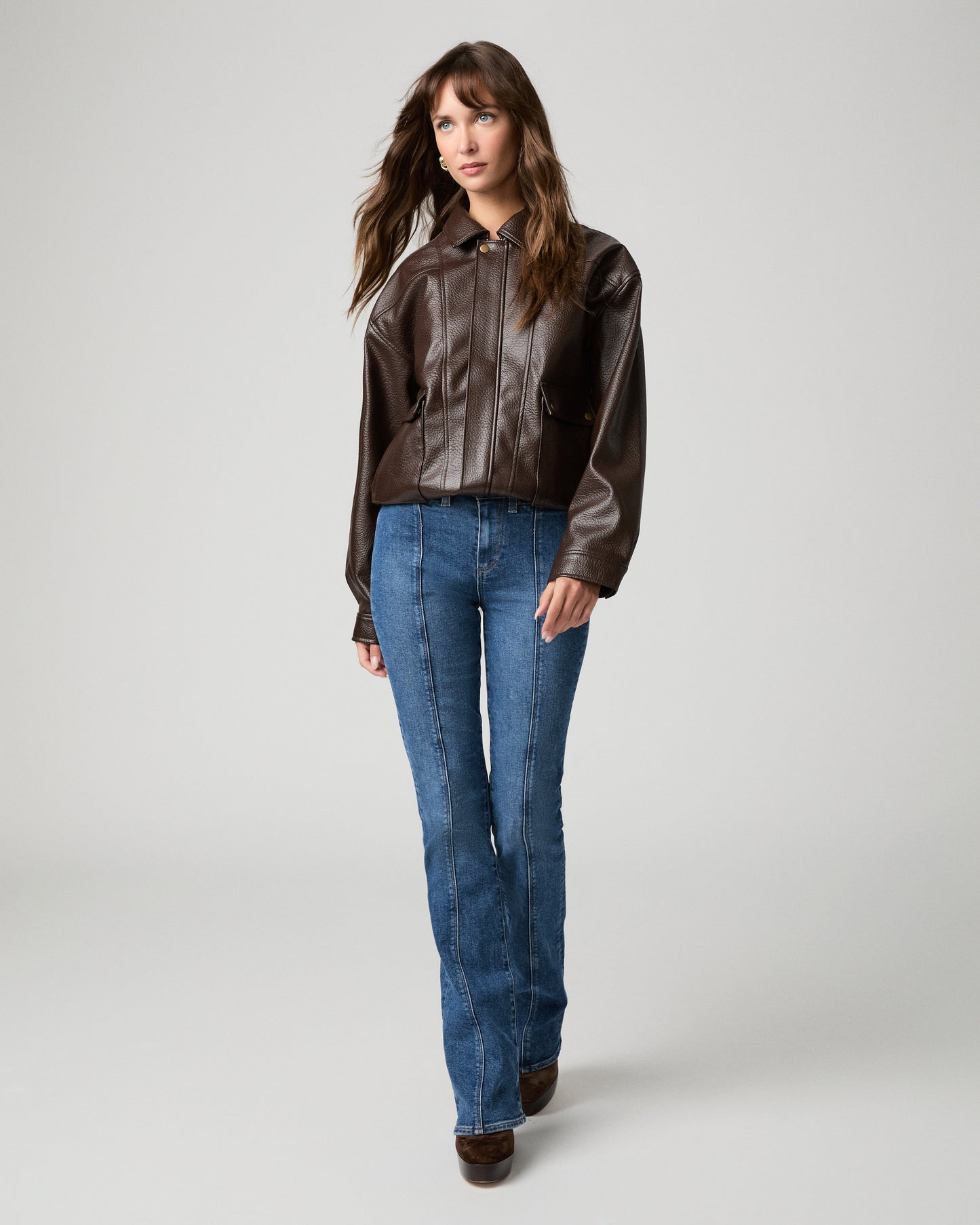 Woman in a brown jacket with blue jeans and a white background
