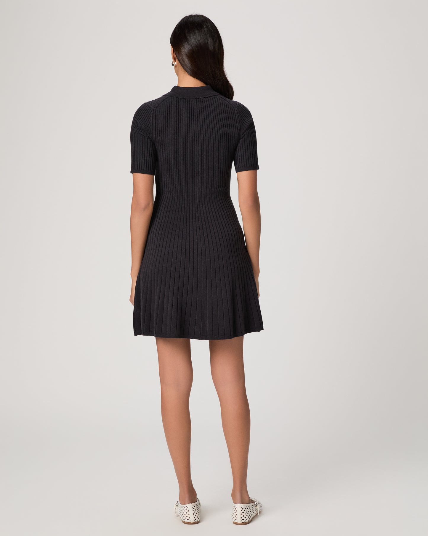 Woman wearing a black dress and white flats on a white background