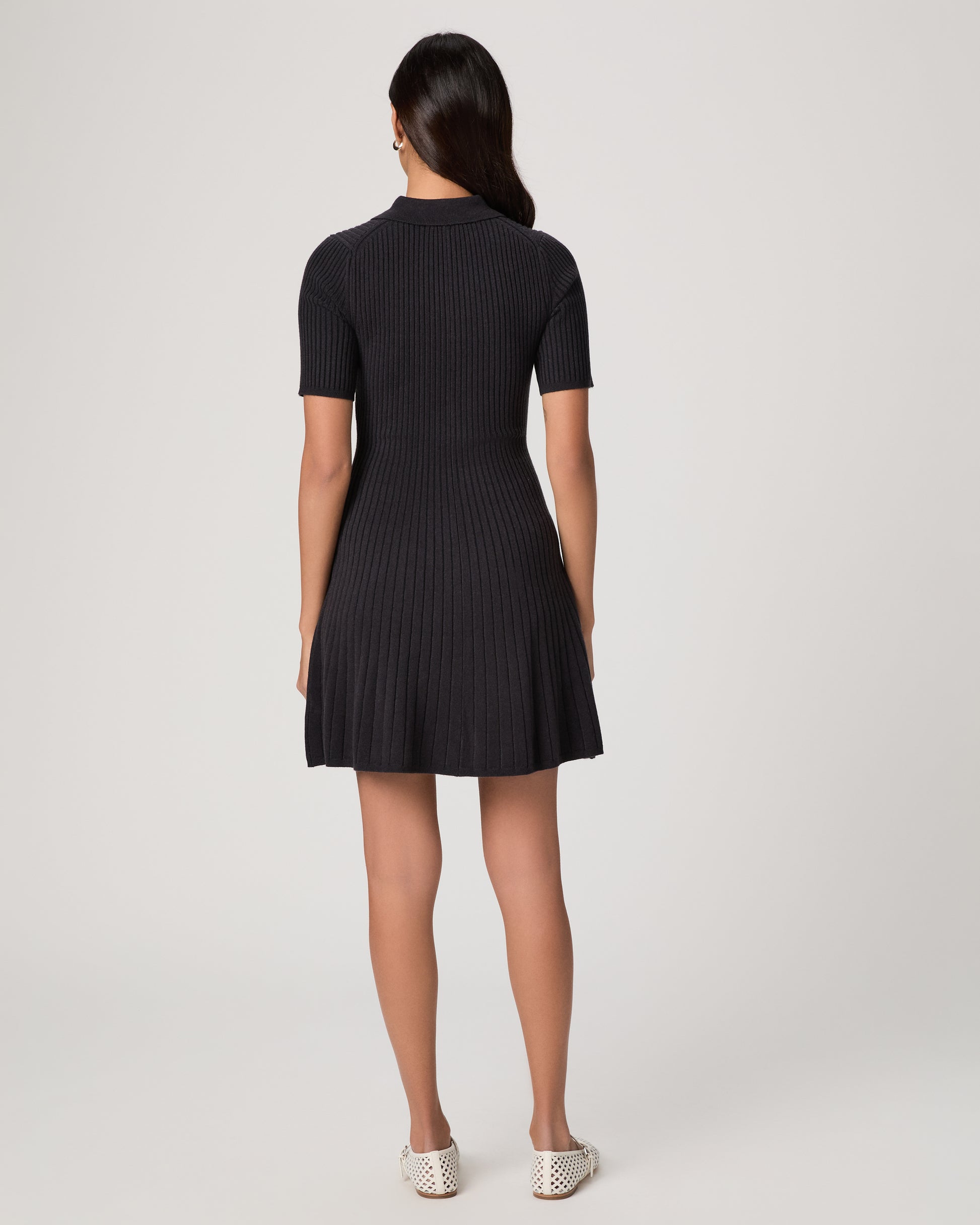 Woman wearing a black dress and white flats on a white background