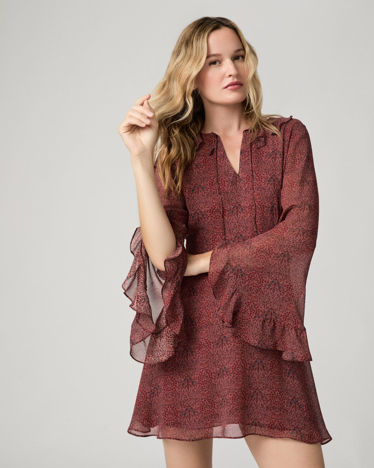 Full-length front view of a woman wearing the garnet floral-print Elspeth Dress with ruffled bell sleeves, paired with tan suede boots.