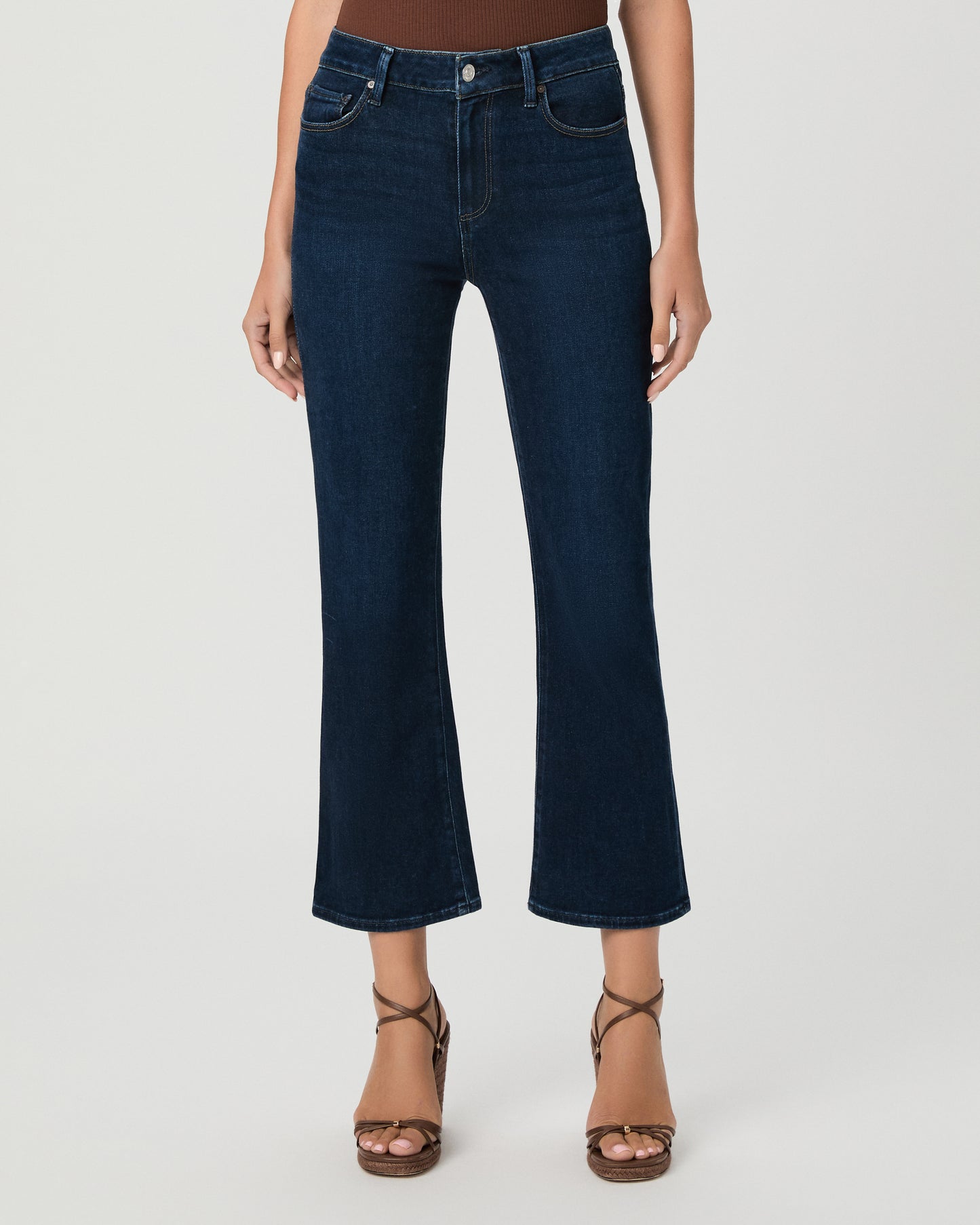 Woman wearing an off the shoulder brown top paired with dark blue jeans and brown wedges against a white background