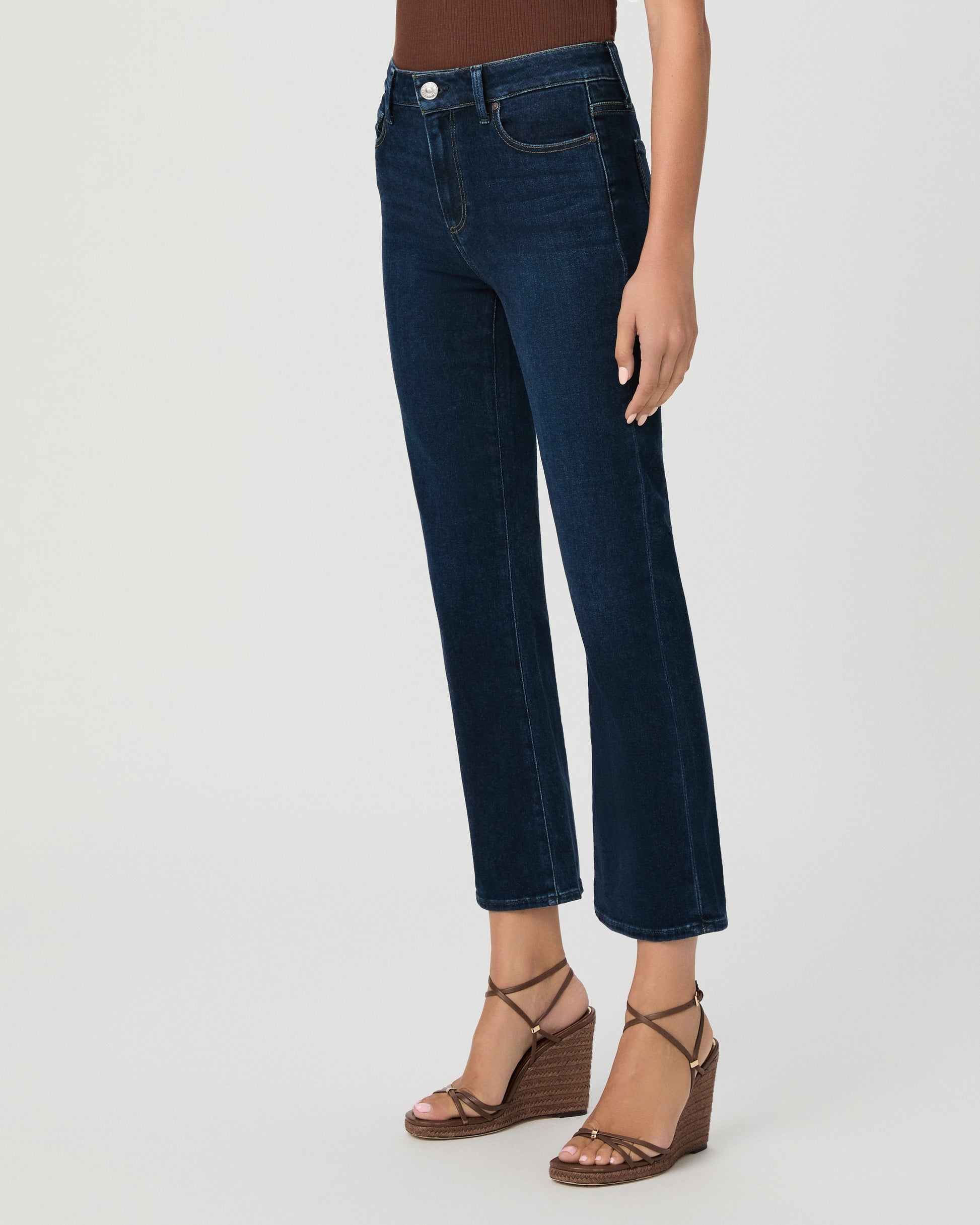 Woman wearing an off the shoulder brown top paired with dark blue jeans and brown wedges against a white background
