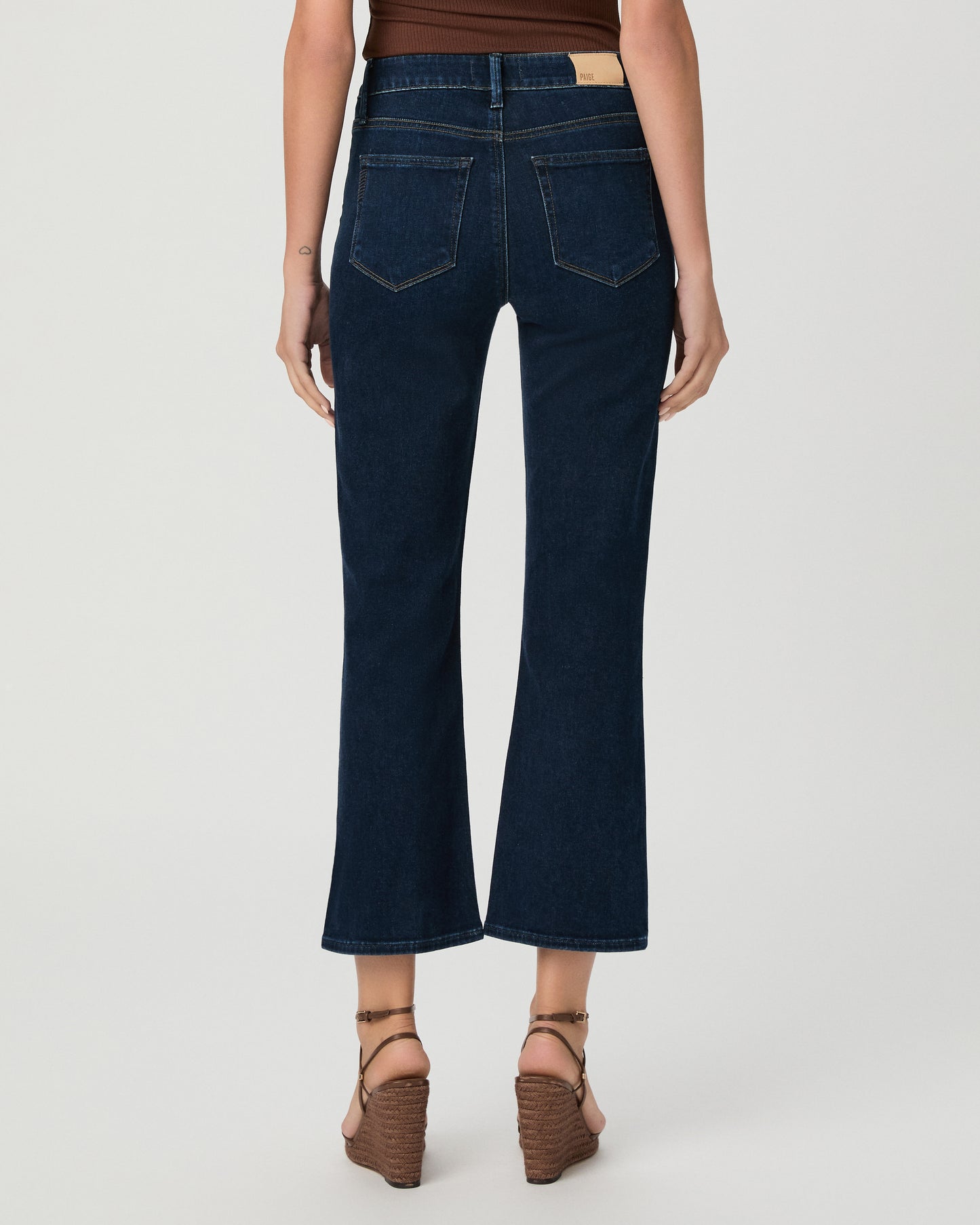 Woman wearing an off the shoulder brown top paired with dark blue jeans and brown wedges against a white background