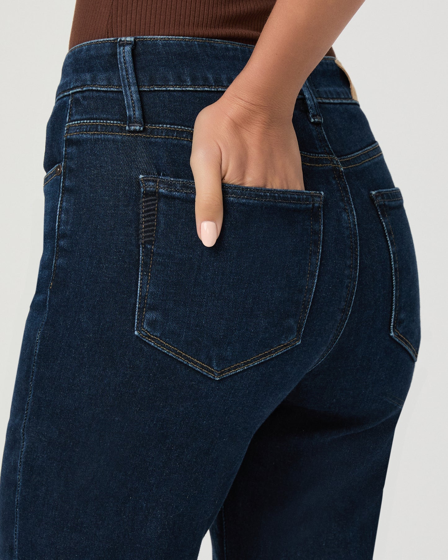 Woman wearing an off the shoulder brown top paired with dark blue jeans and brown wedges against a white background