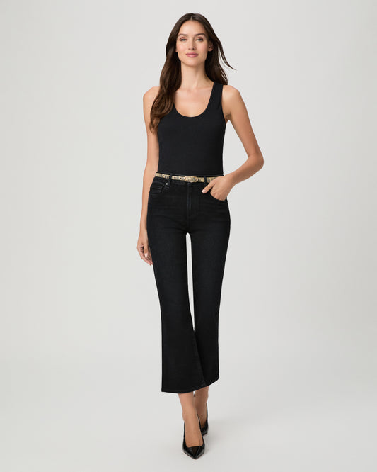 Woman wearing a black top paired with black  jeans and black heels against a white background