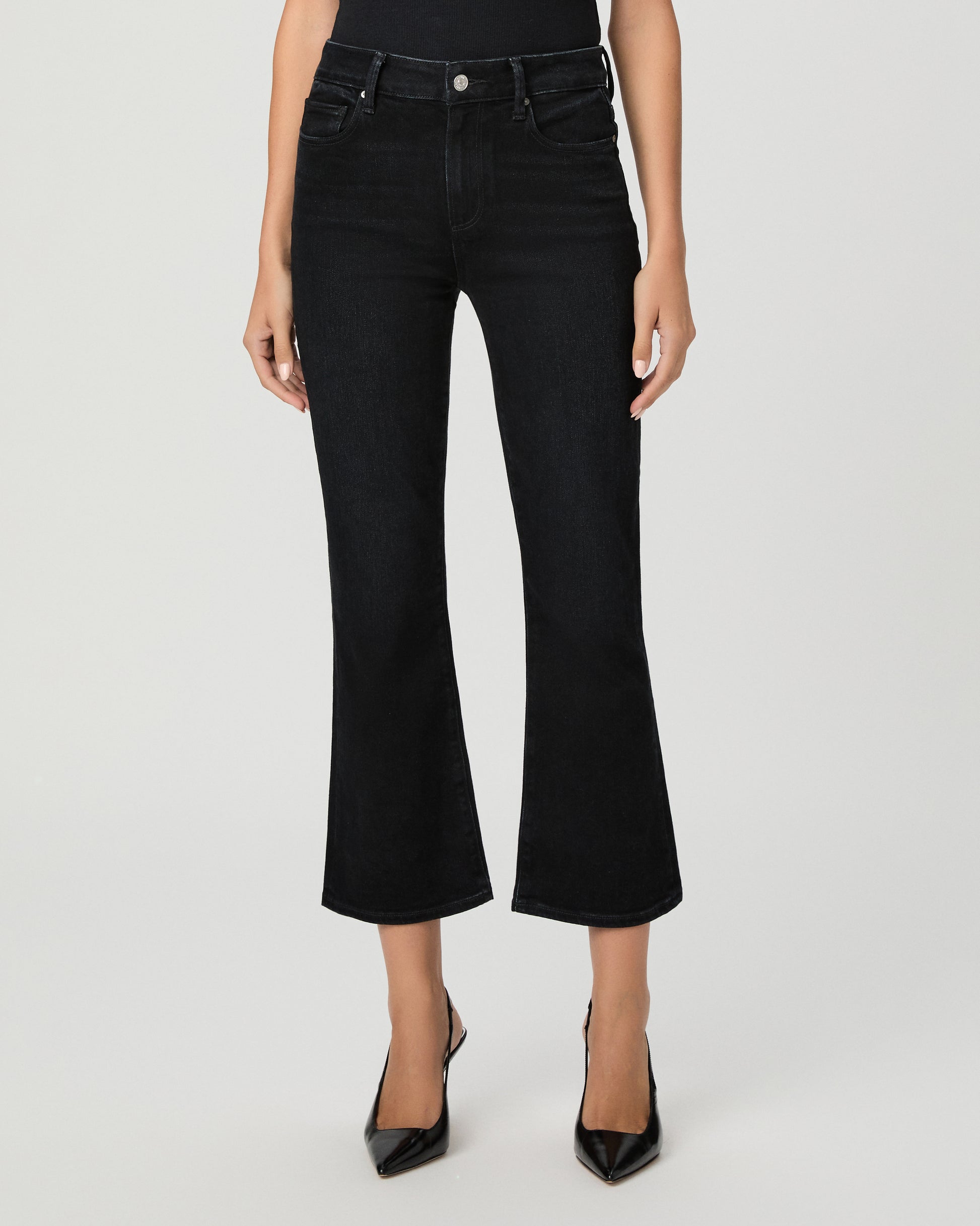 Woman wearing a black top paired with black  jeans and black heels against a white background