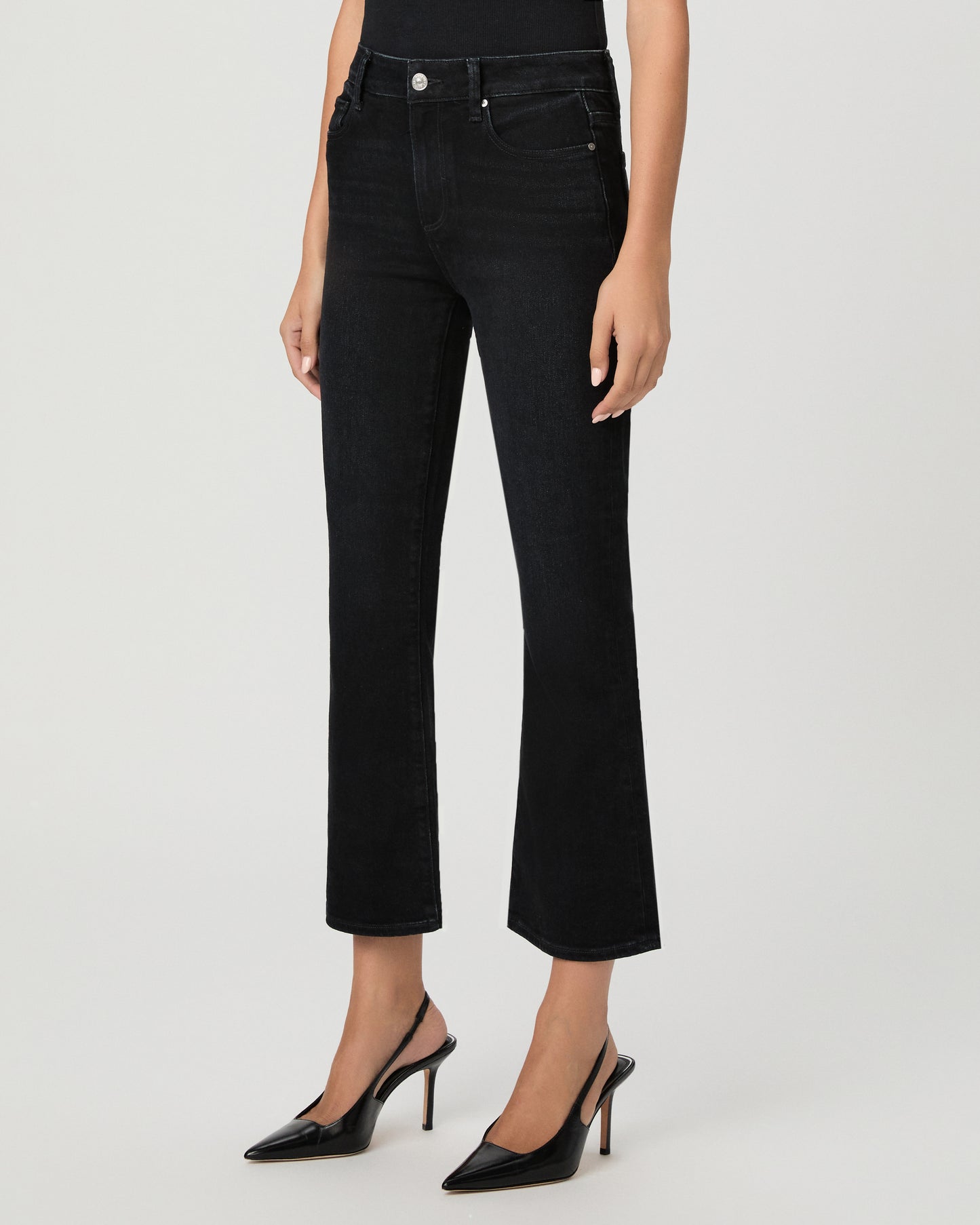 Woman wearing a black top paired with black  jeans and black heels against a white background