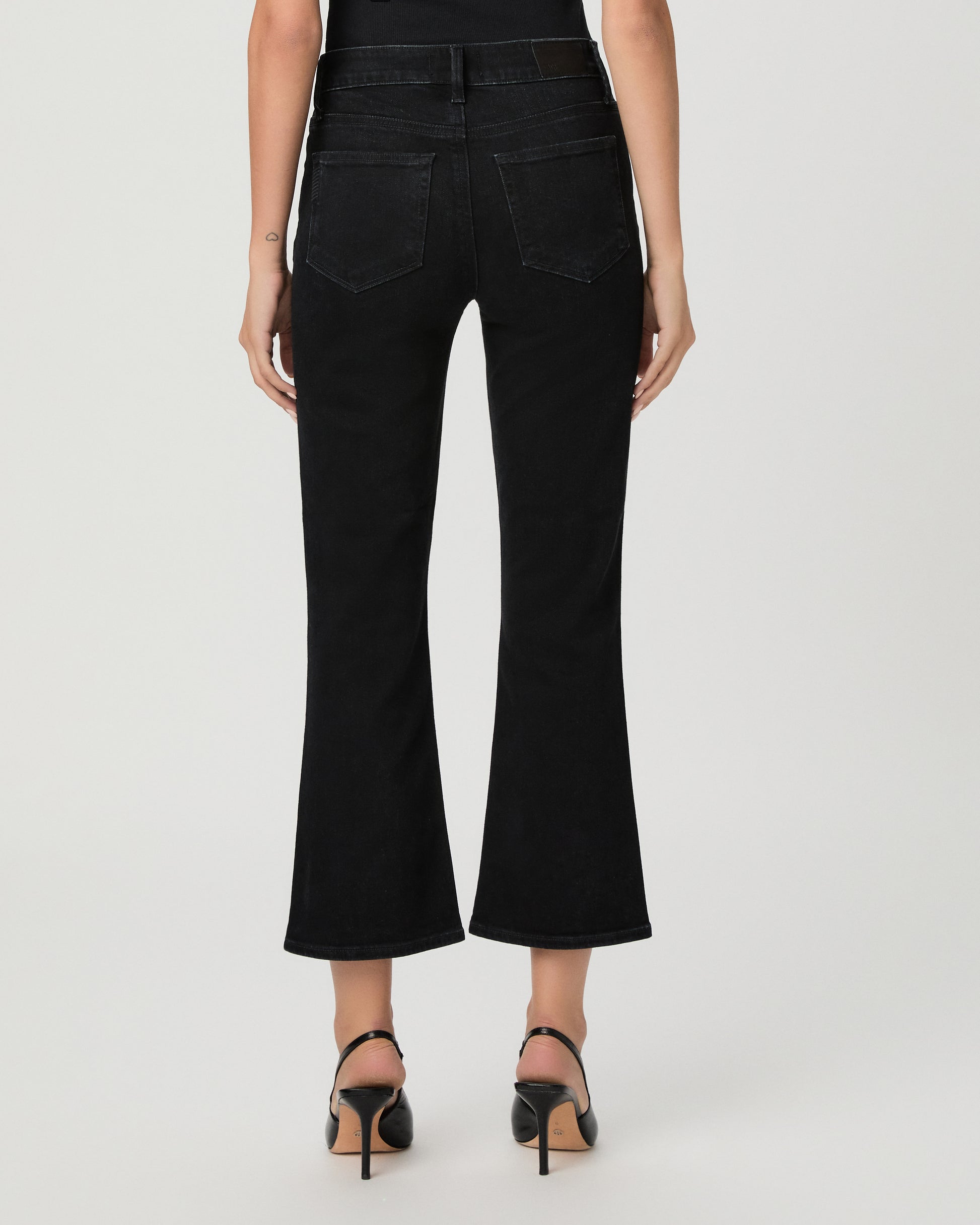 Woman wearing a black top paired with black  jeans and black heels against a white background