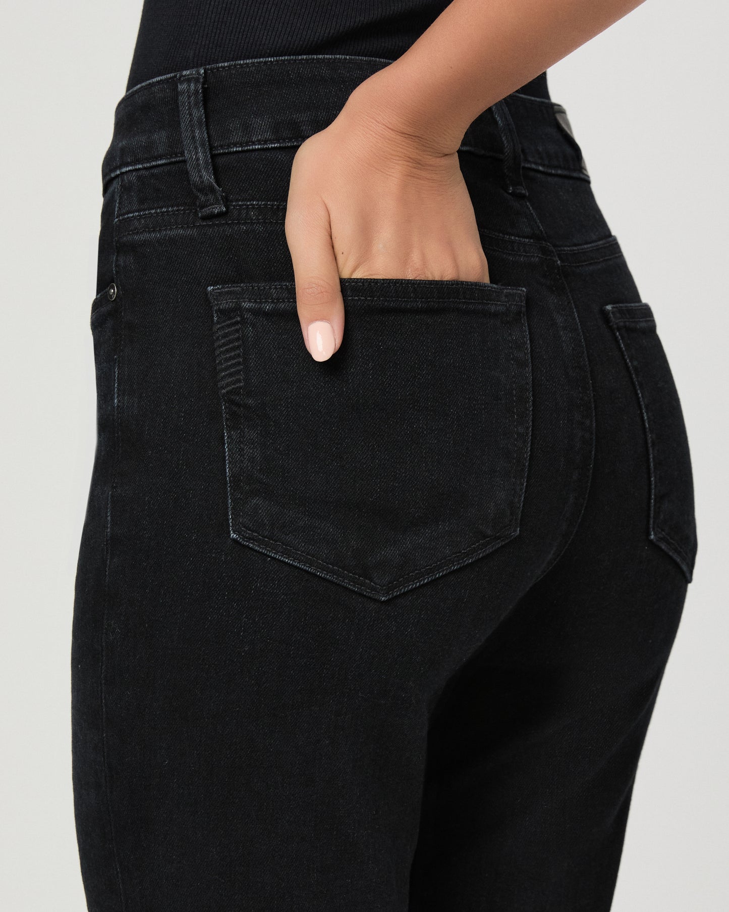 Woman wearing a black top paired with black  jeans and black heels against a white background