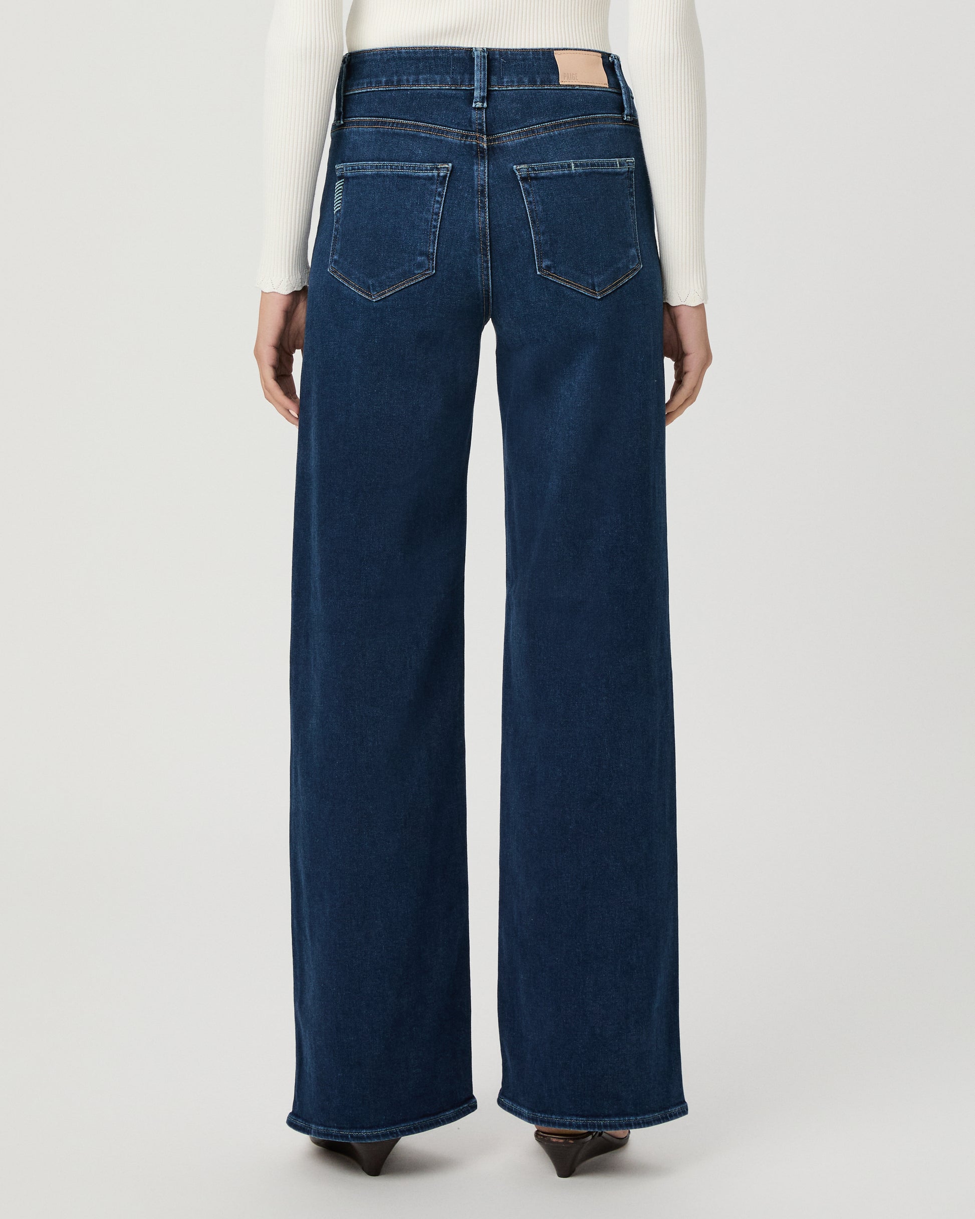 A woman modeling a cream long-sleeve button-front cardigan and dark blue wide-leg jeans against a light gray studio background.