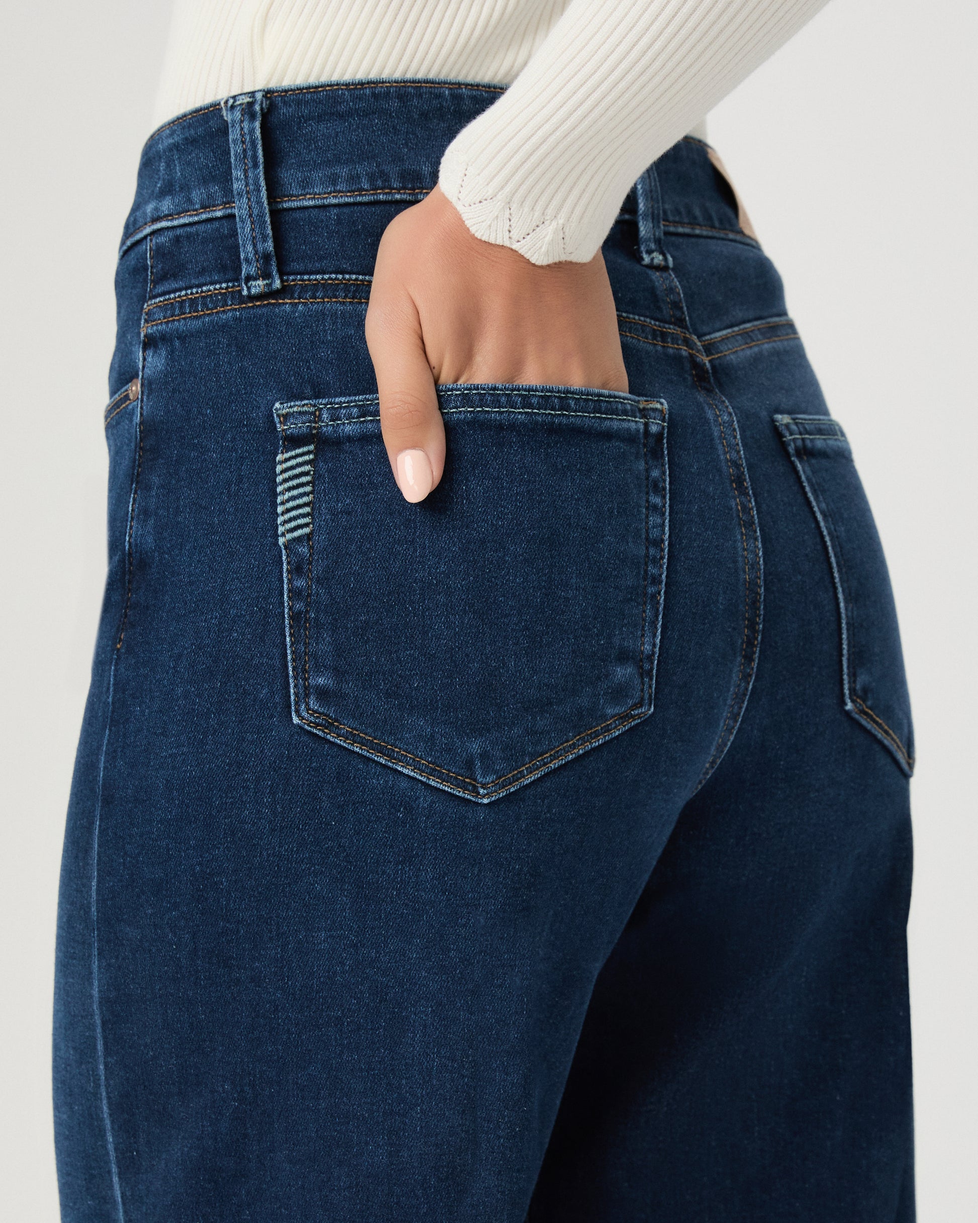 A woman modeling a cream long-sleeve button-front cardigan and dark blue wide-leg jeans against a light gray studio background.