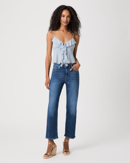Woman wearing a blue blouse paired with medium wash jeans and gold wedges against a white background
