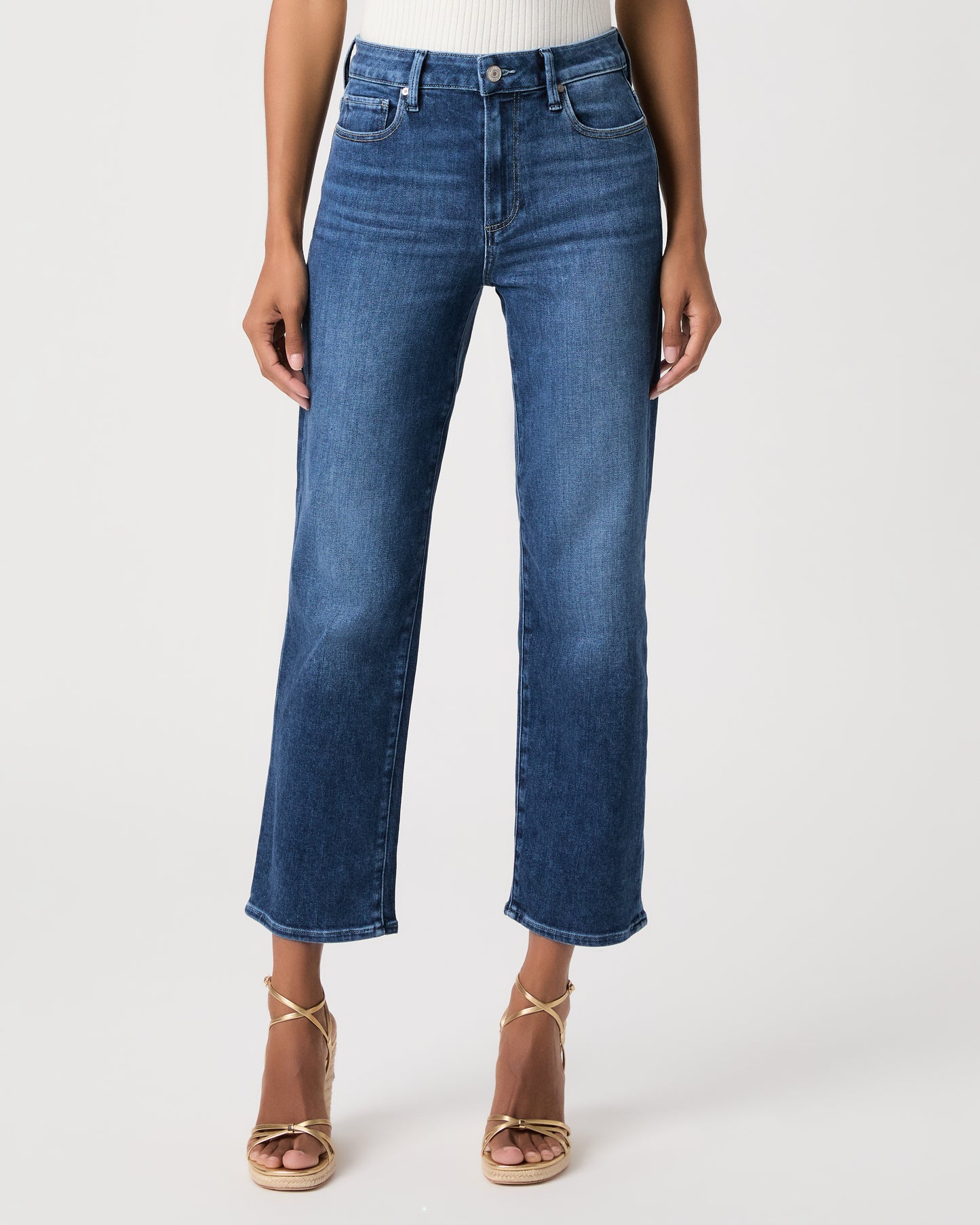 Woman wearing a white top paired with medium wash jeans and gold wedges against a white background