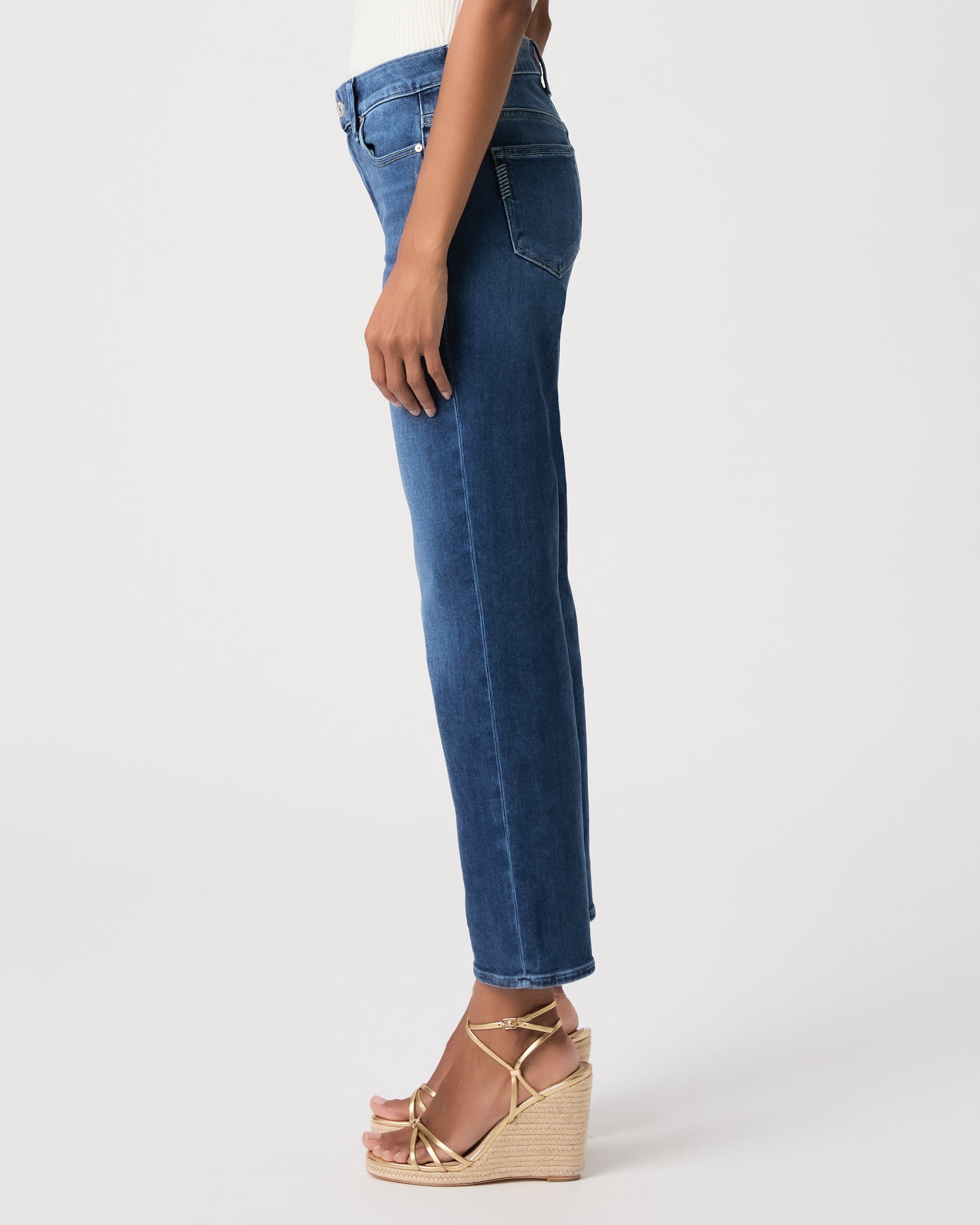 Woman wearing a white top paired with medium wash jeans and gold wedges against a white background