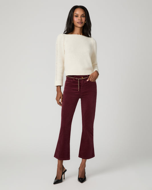 Full-length front view of a woman wearing an ivory ribbed sweater and burgundy corduroy cropped bootcut jeans with button-front detail, paired with black pointed-toe heels.