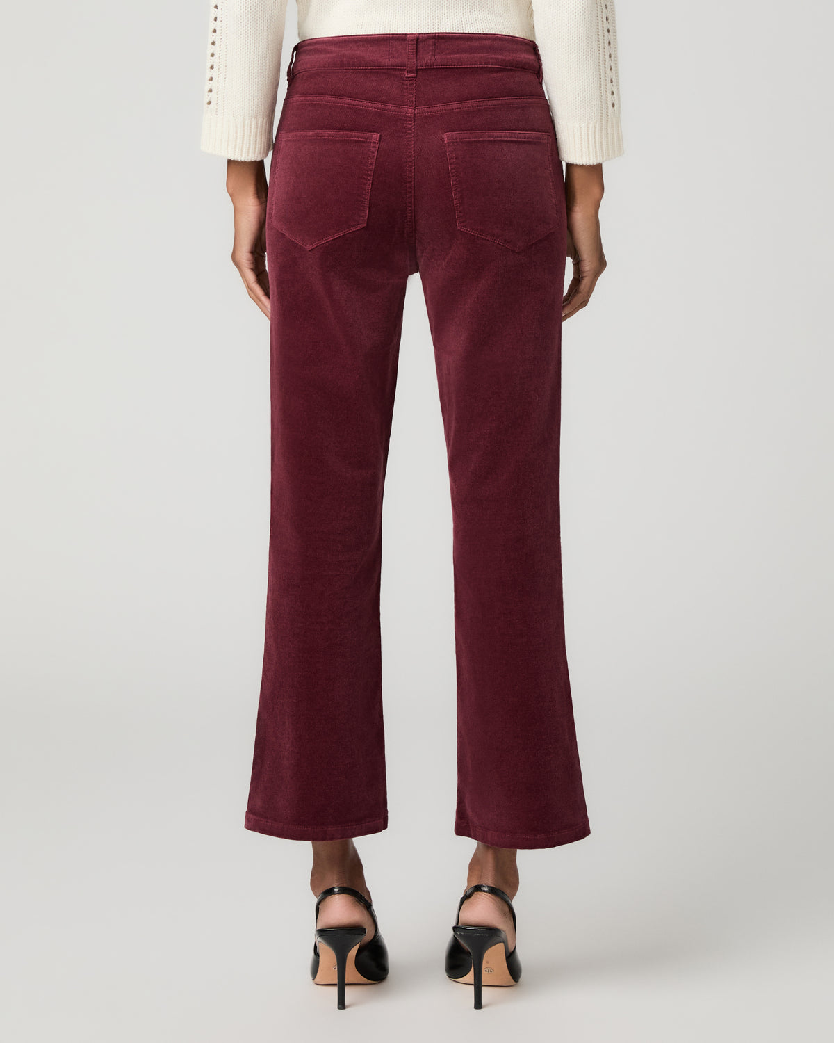 Close-up back view of burgundy corduroy cropped bootcut jeans showing a patch back pocket, paired with black ankle-strap heels.