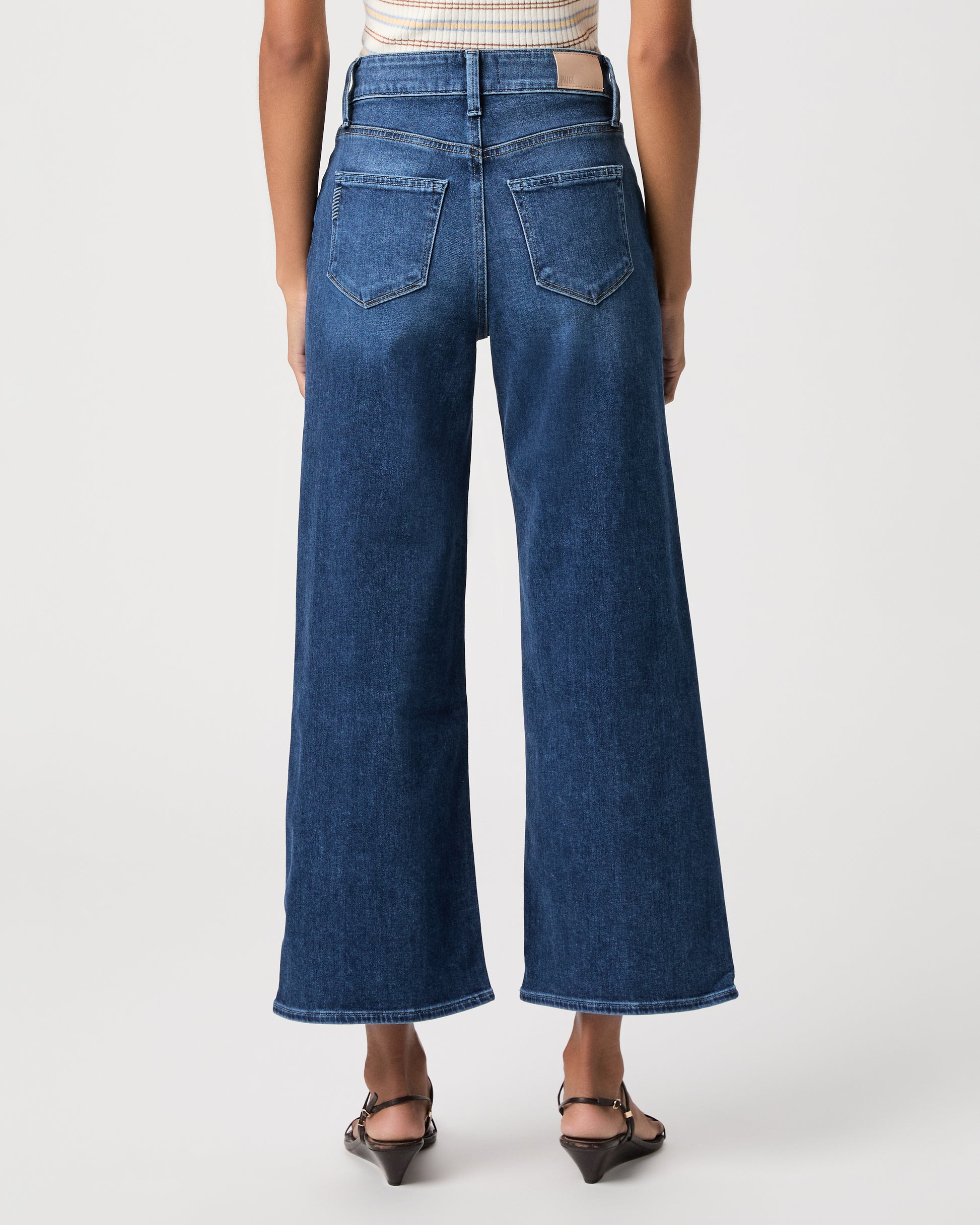 women wearing a white stripped top paired with blue jeans and black sandals against a white background 