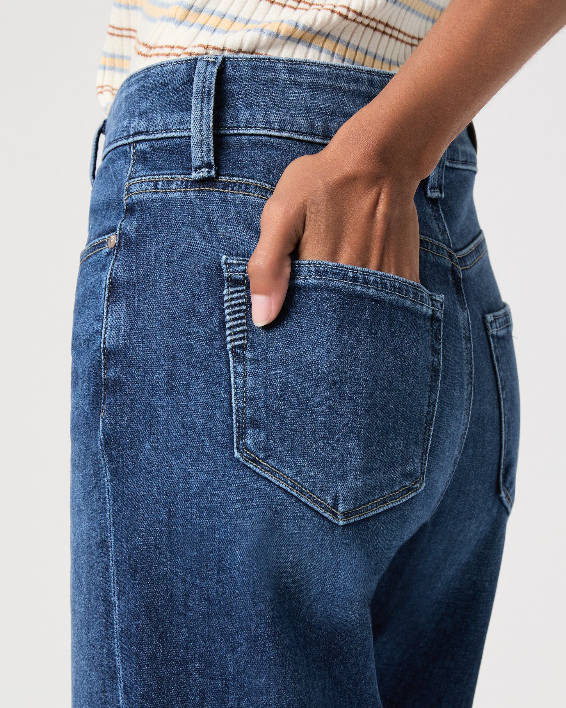 women wearing a white stripped top paired with blue jeans and black sandals against a white background 
