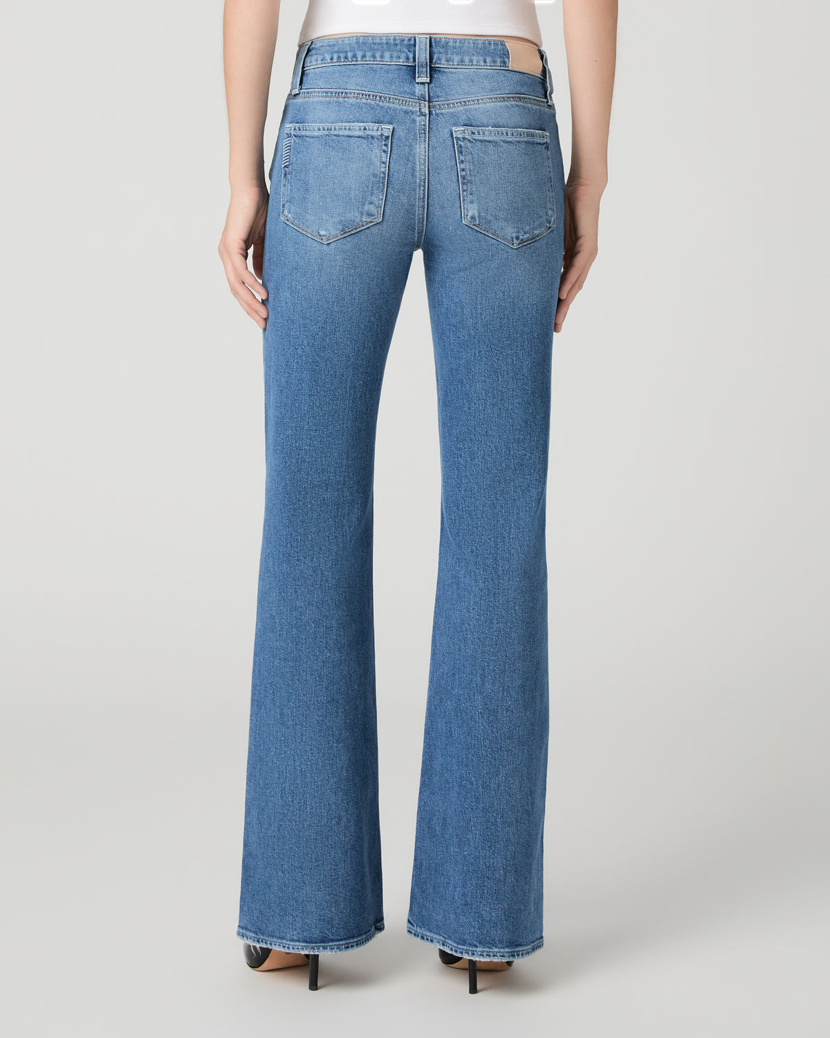 Women wearing a white top paired with blue jean and black heels against a white background