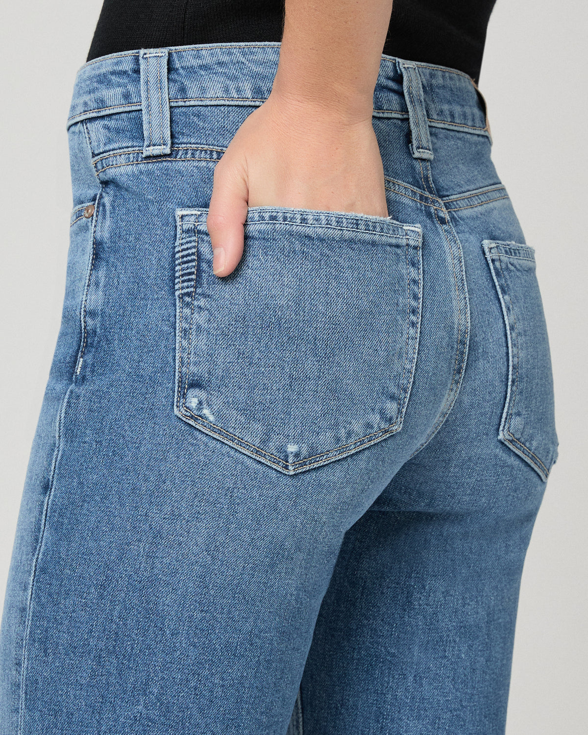 Women wearing a black vest top paired with blue jean against a white background