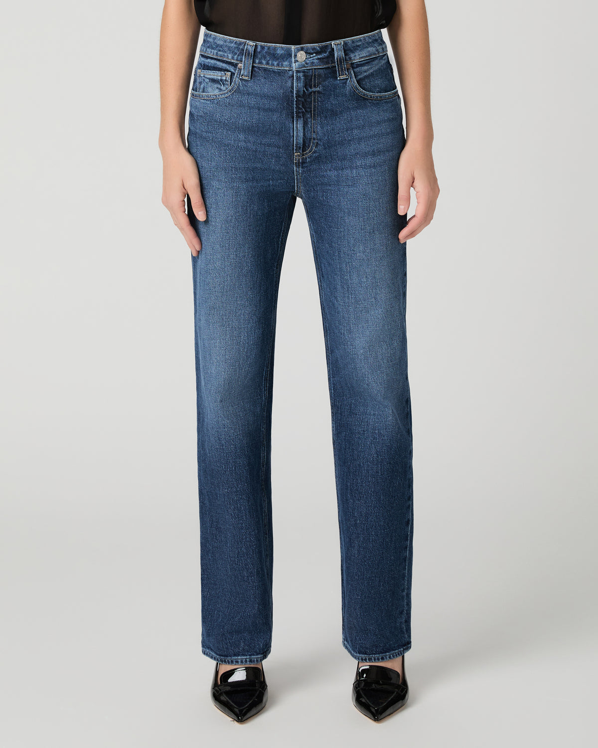 Women wearing a black top paired with blue jean and black heels against a white background