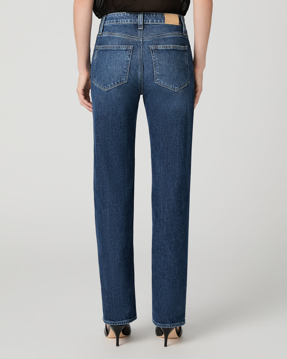 Women wearing a black top paired with blue jean and black heels against a white background