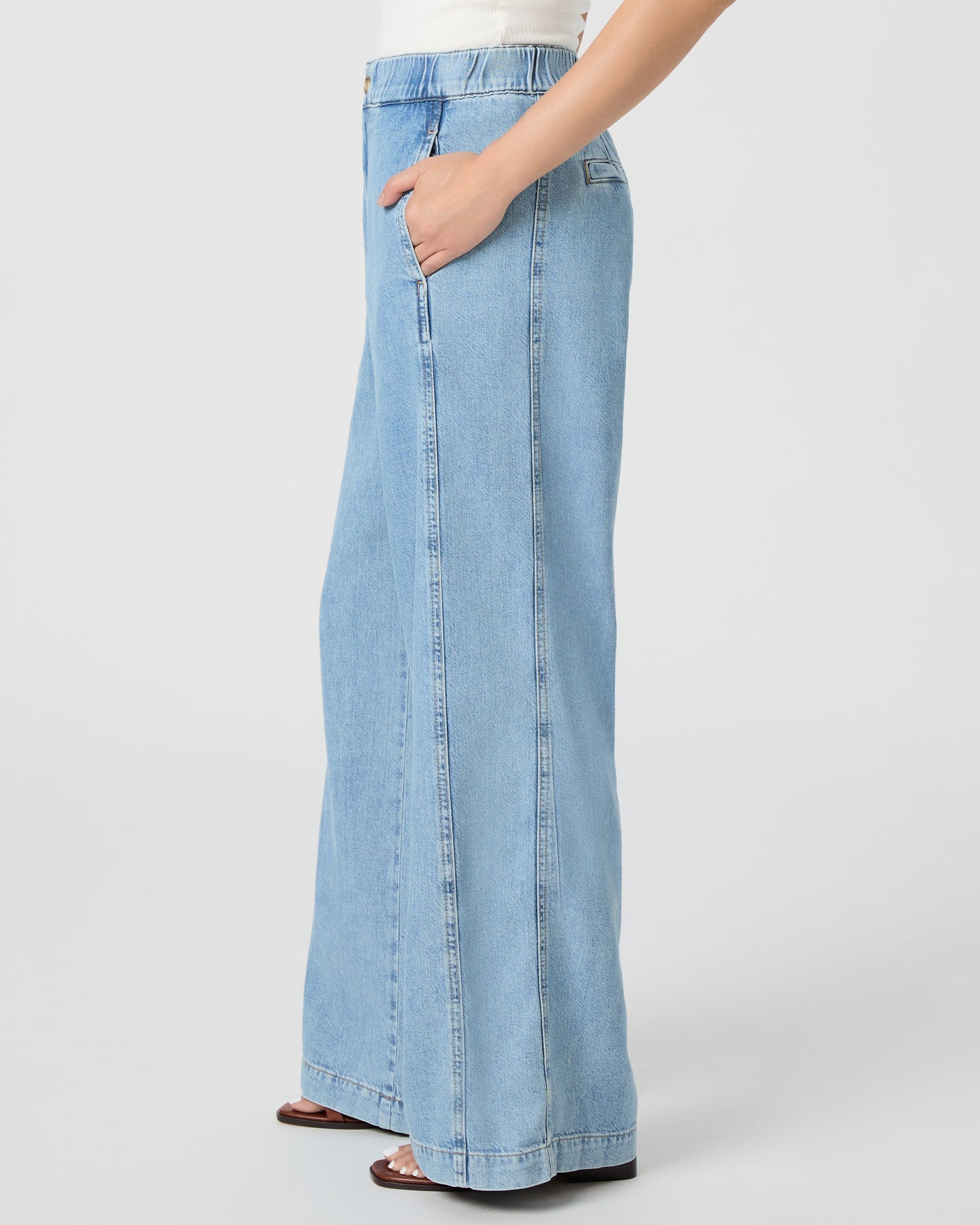Woman wearing a white tank and blue jeans paired with brown sandals on a white background