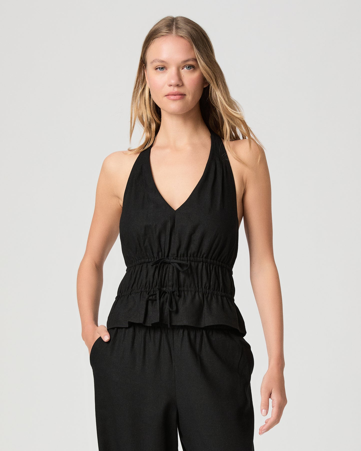 Woman wearing a black halter neck top with black pant against a plain background