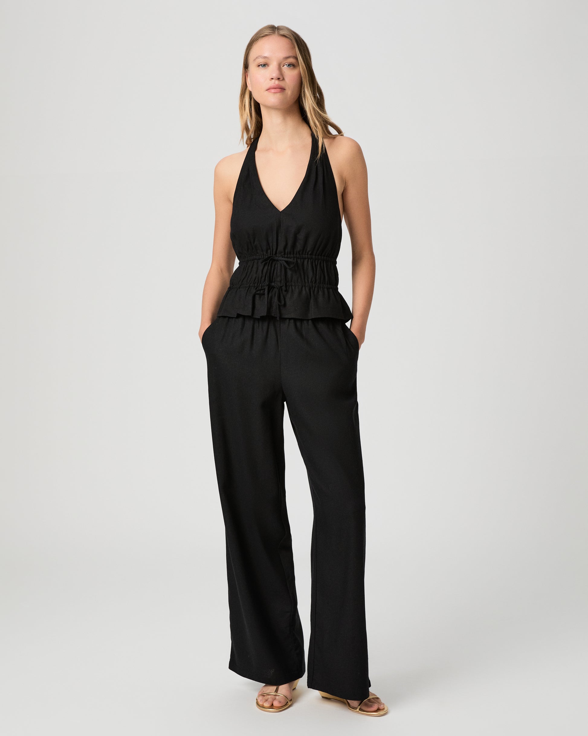 Woman wearing a black halter neck top with black pant against a plain background