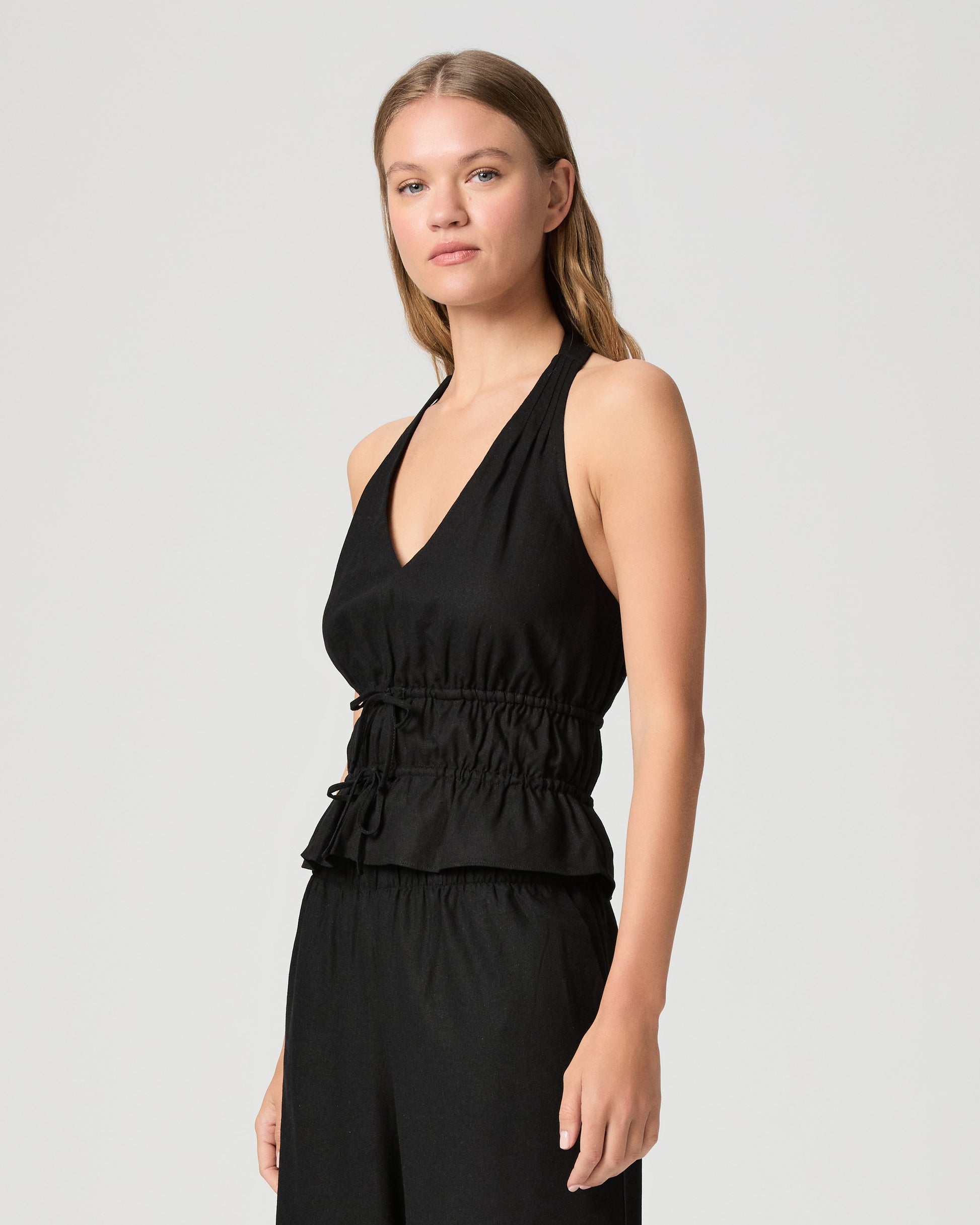 Woman wearing a black halter neck top with black pant against a plain background