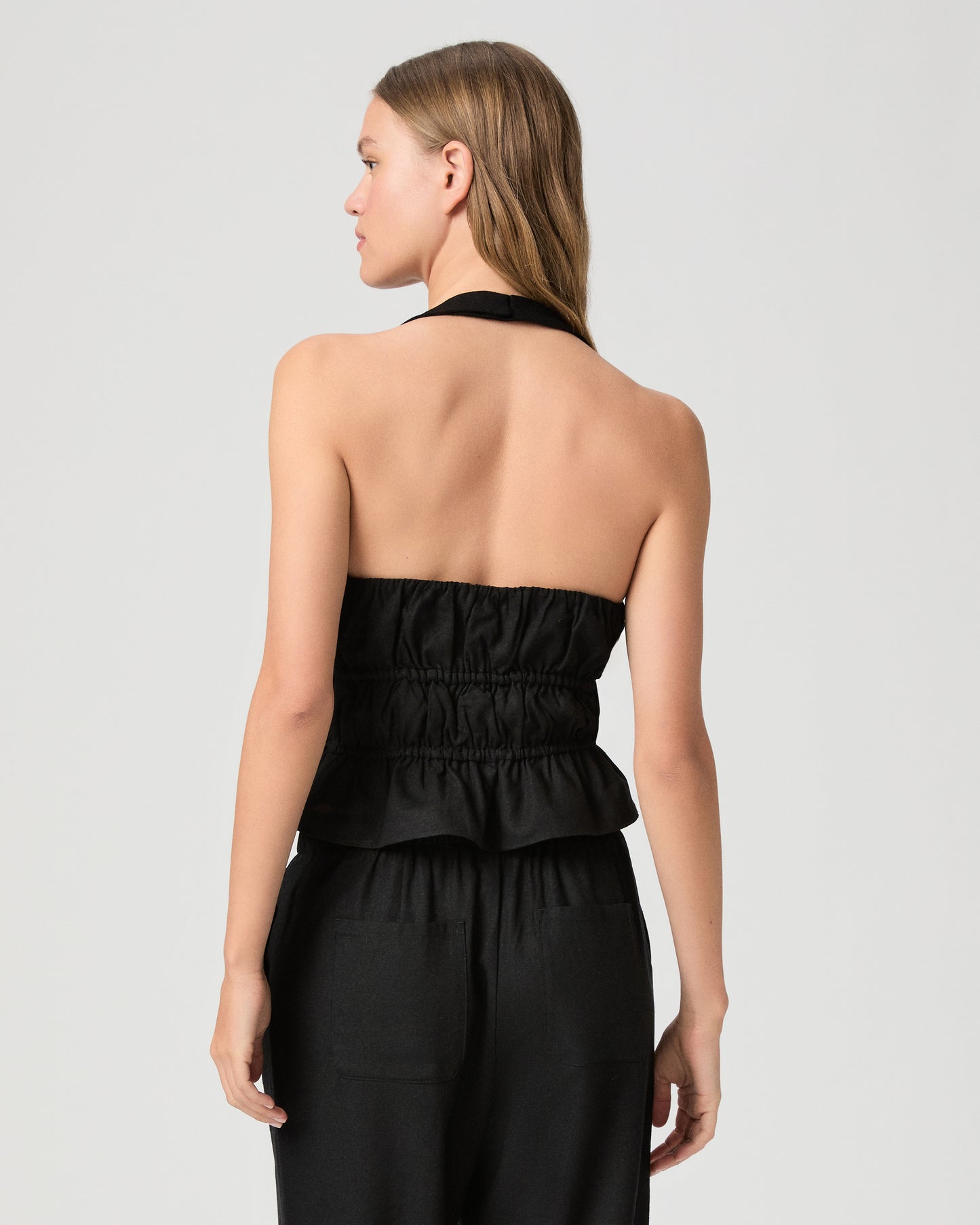 Woman wearing a black halter neck top with black pant against a plain background