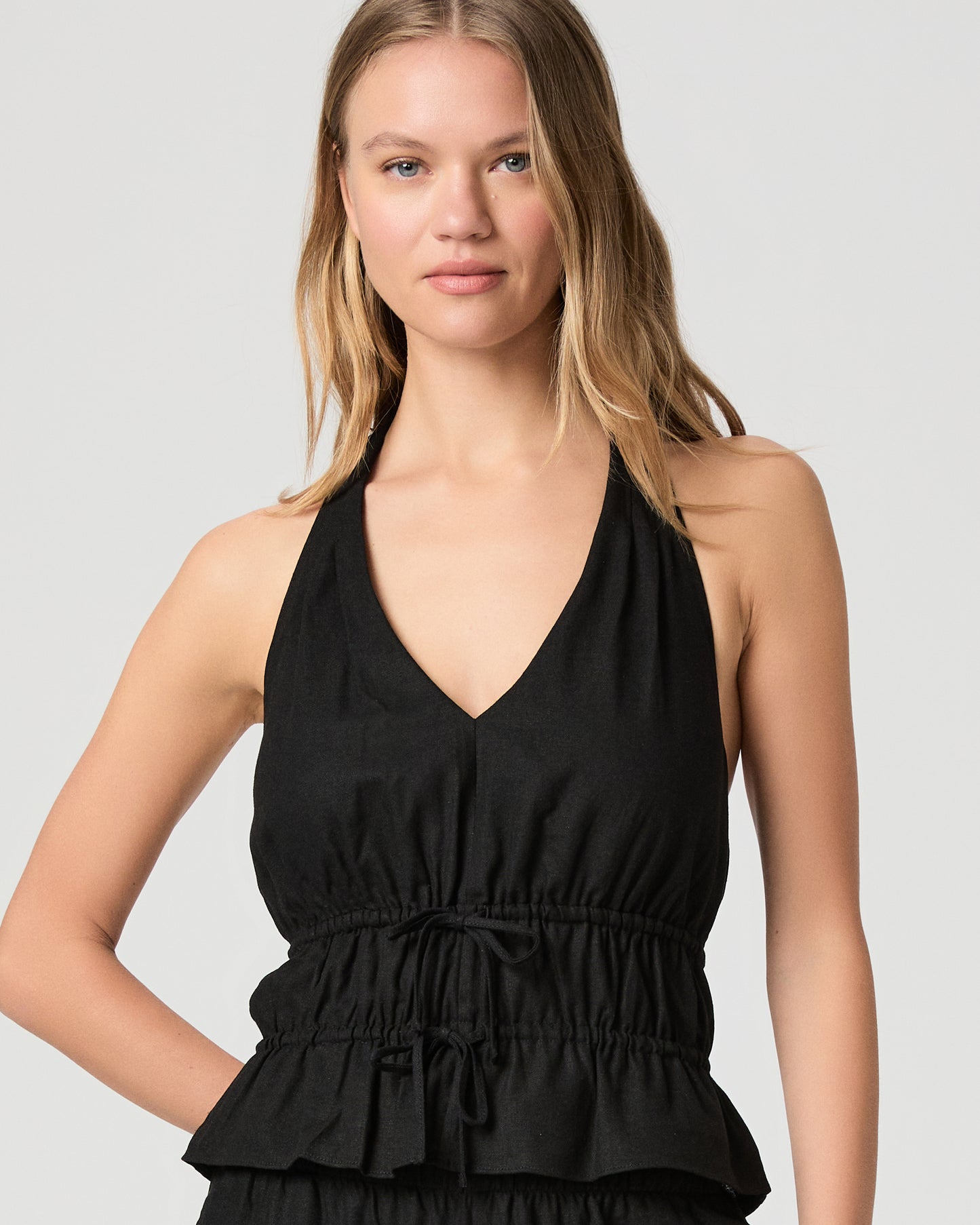 Woman wearing a black halter neck top with black pant against a plain background