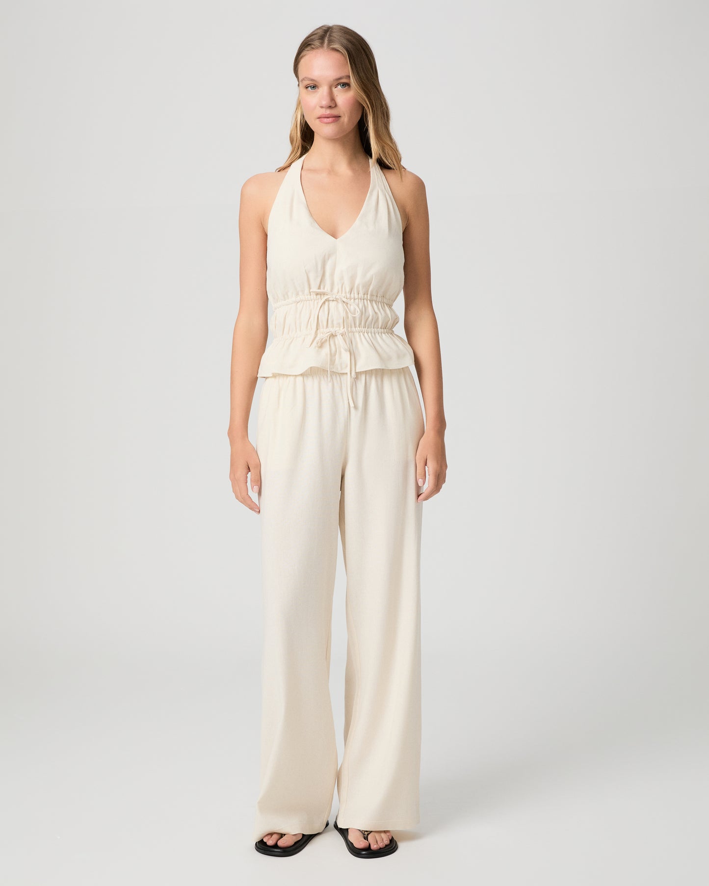 Woman wearing a white halter neck top and white pants against a plain background