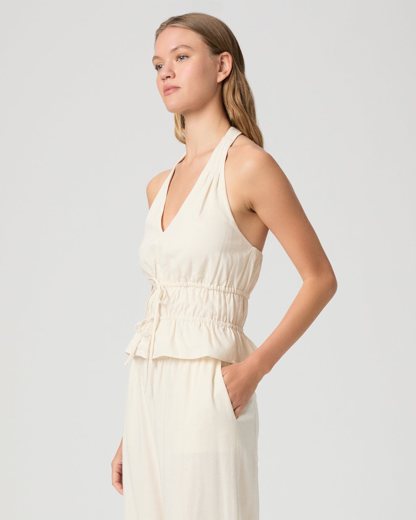 Woman wearing a white halter neck top and white pants against a plain background
