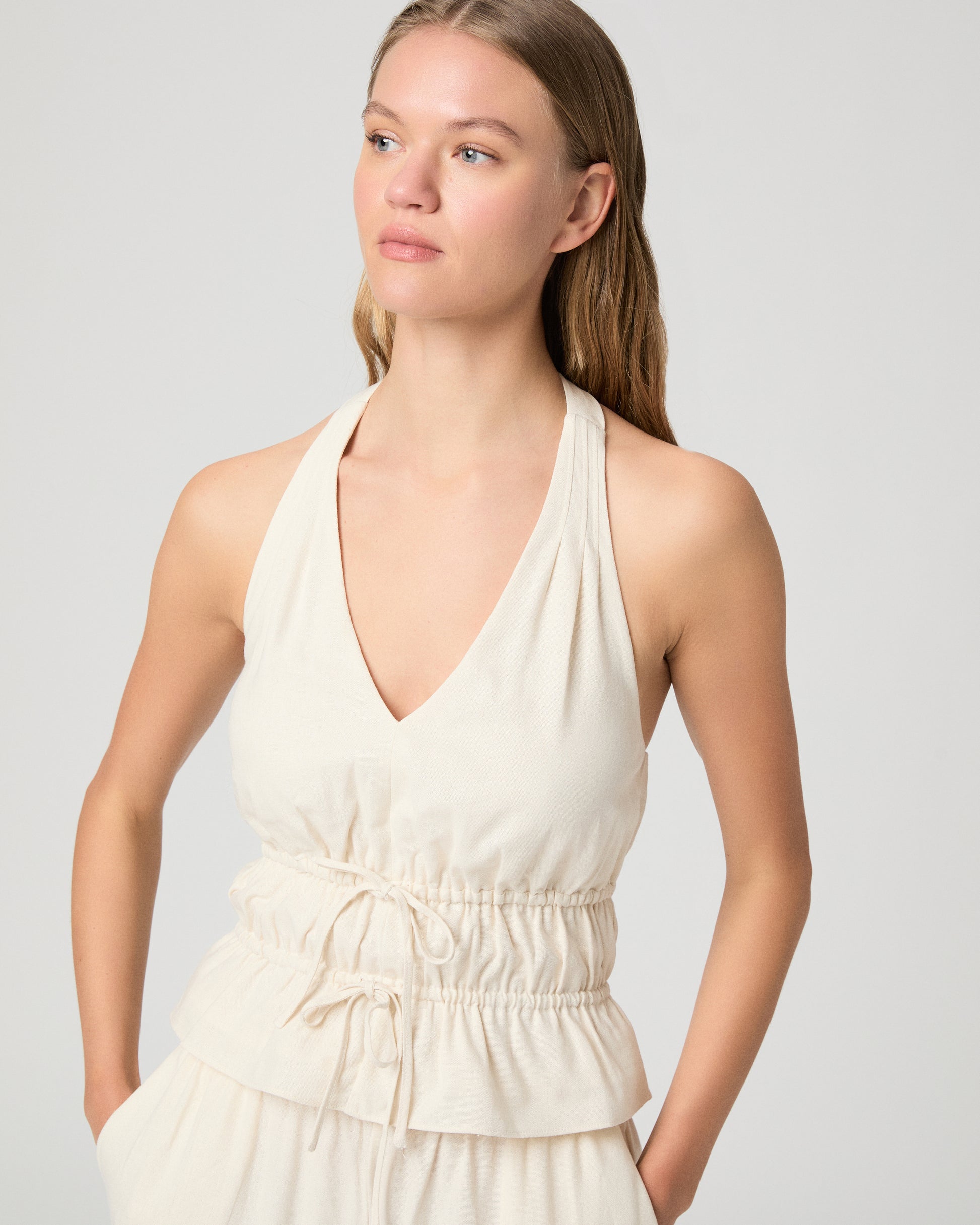 Woman wearing a white halter neck top and white pants against a plain background