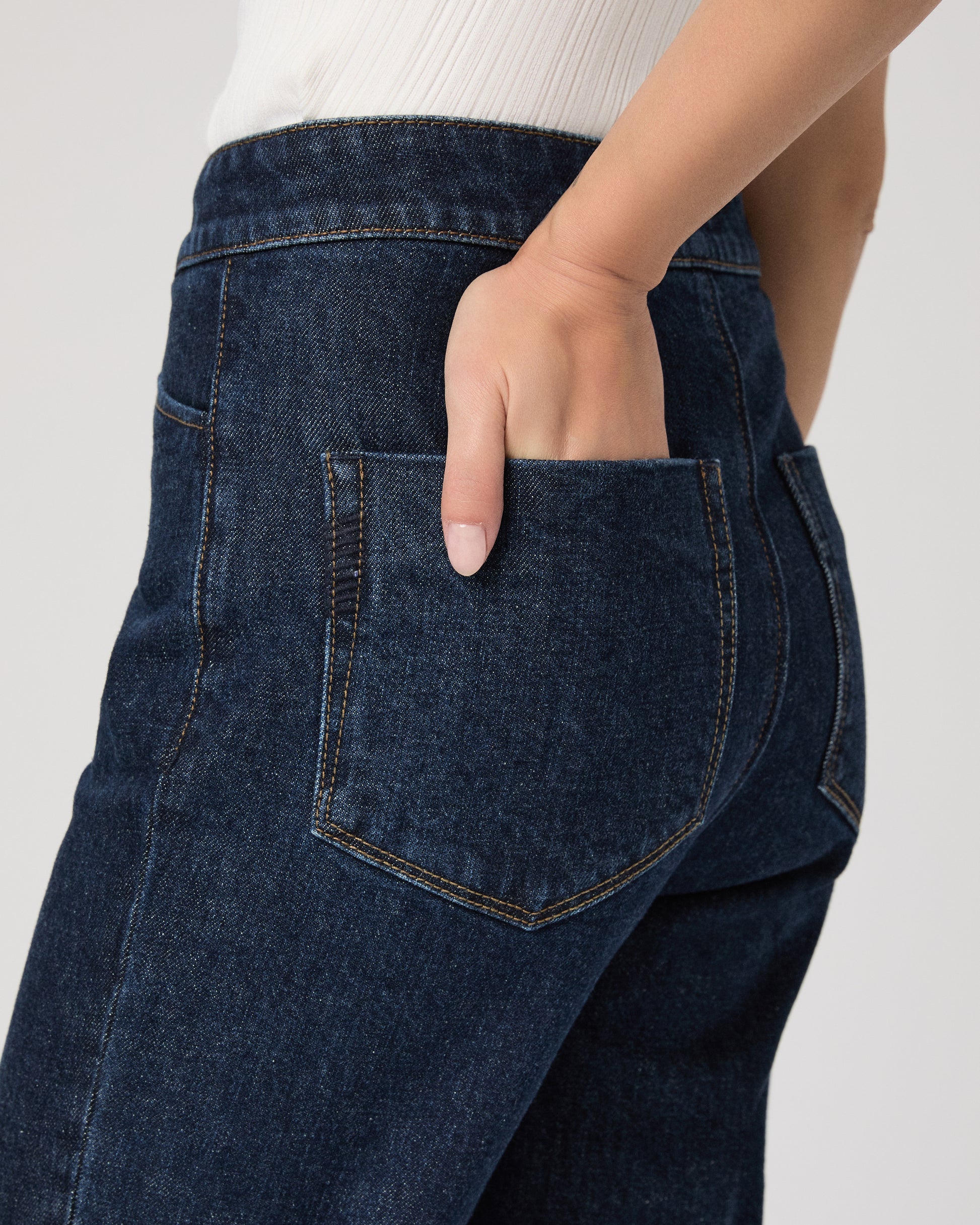 Woman wearing a white sleeveless top and dark blue jeans on white background