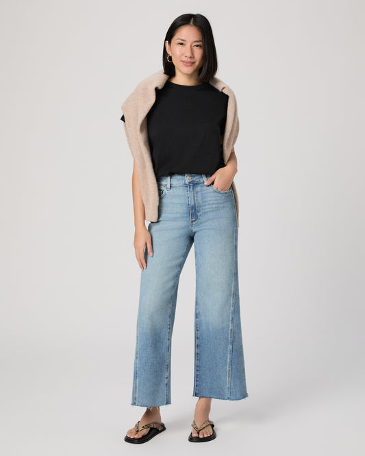 Woman wearing a black top, beige cardigan, and blue jeans on a white background