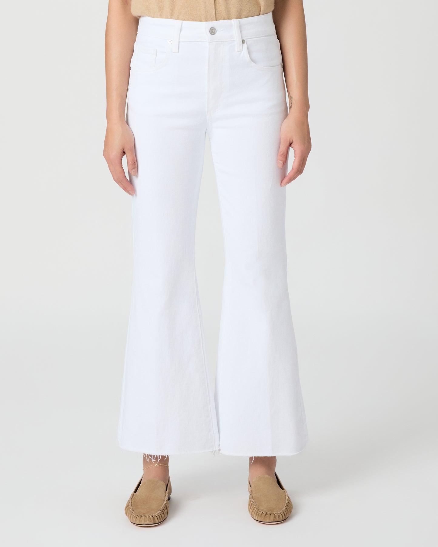 Woman wearing a beige sleeveless top and white pants on a plain background