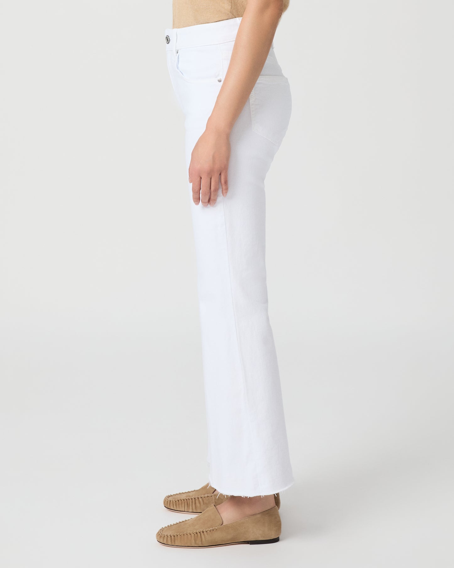 Woman wearing a beige sleeveless top and white pants on a plain background