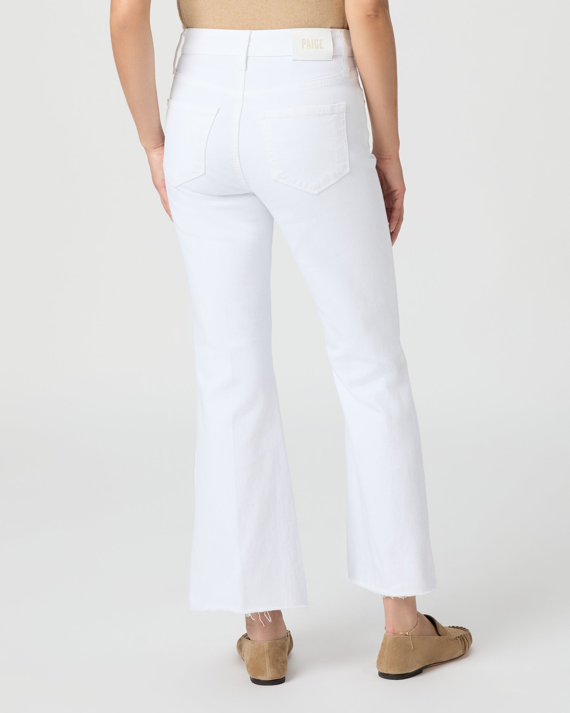 Woman wearing a beige sleeveless top and white pants on a plain background