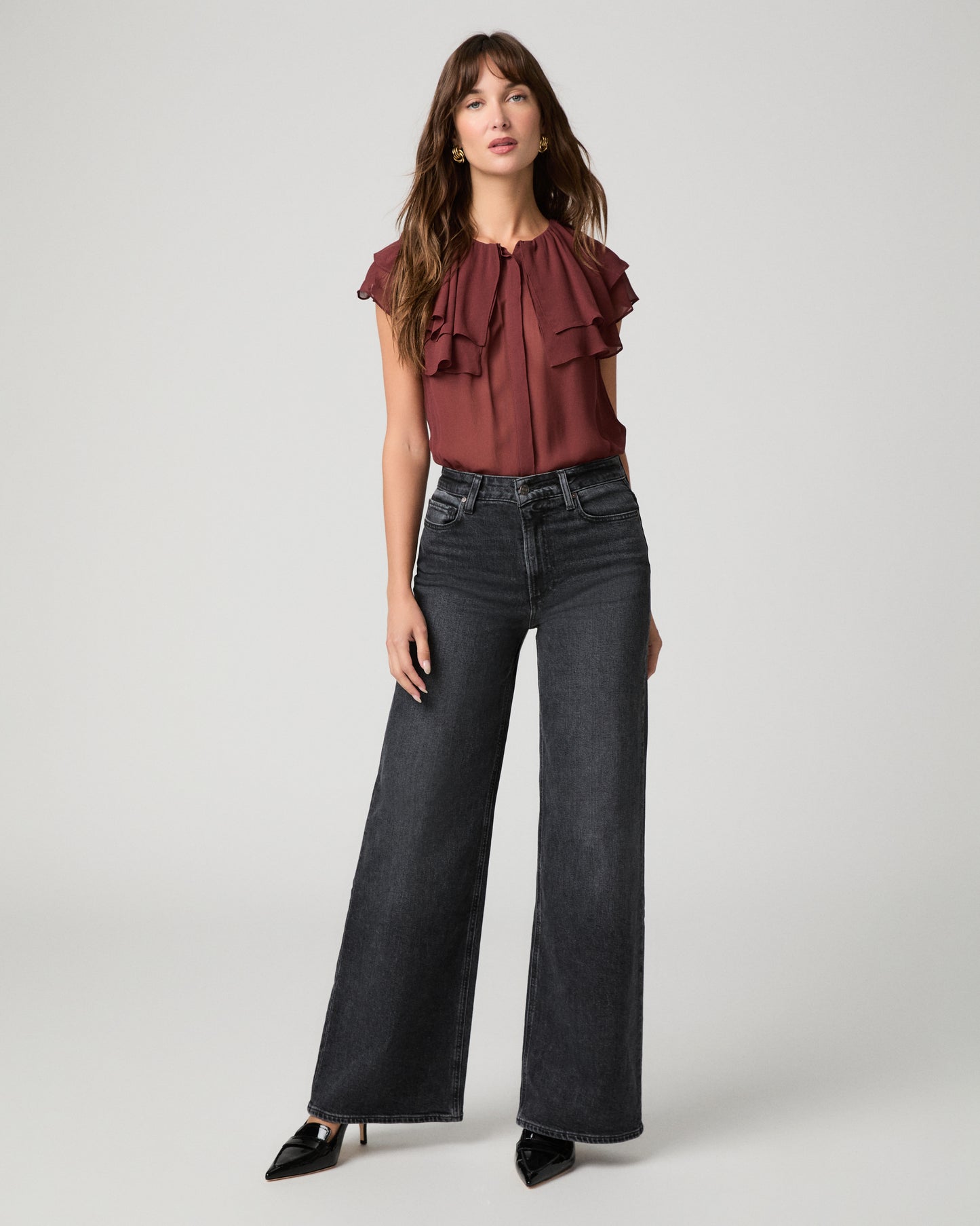 Woman wearing maroon top and black jeans against a white background