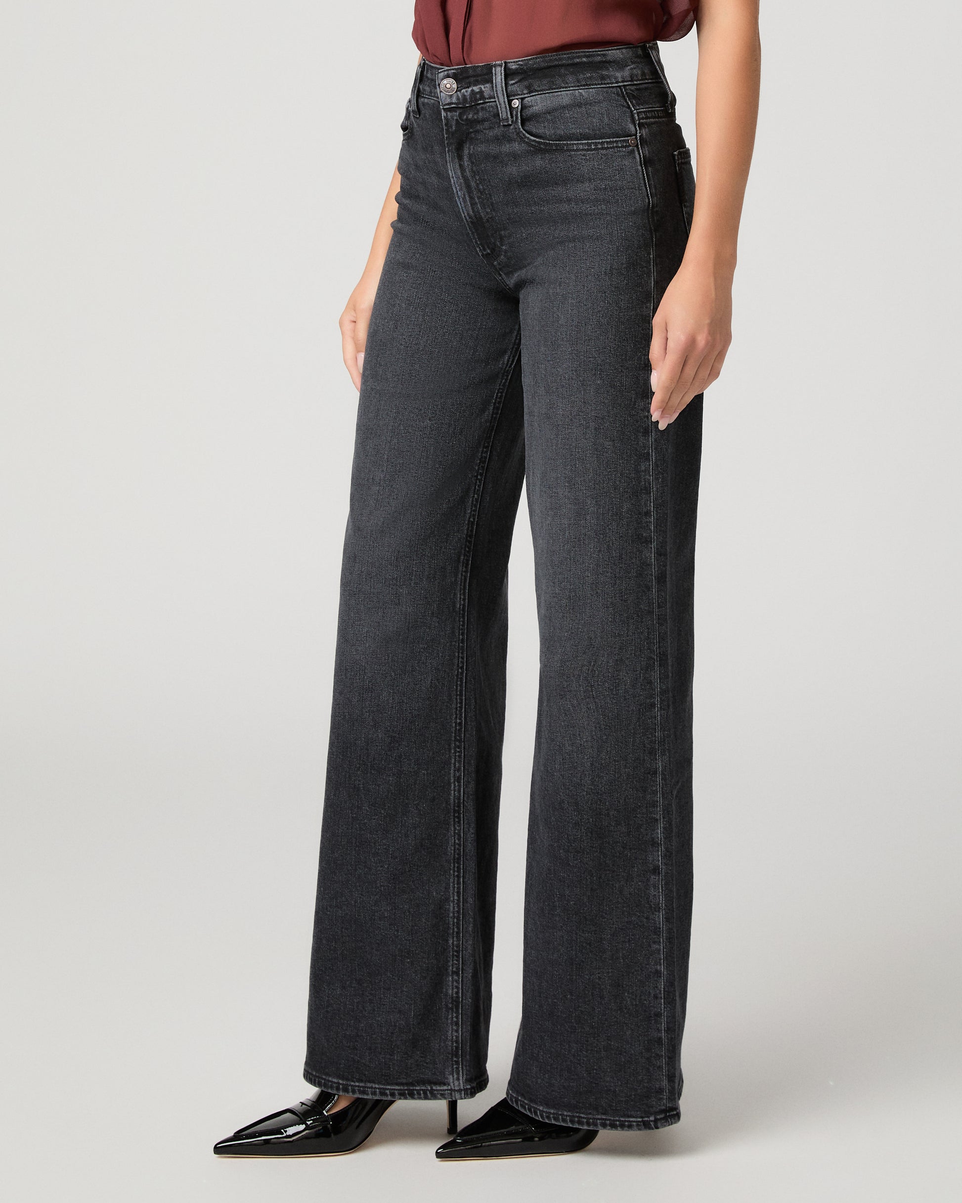 Woman wearing maroon top and black jeans against a white background