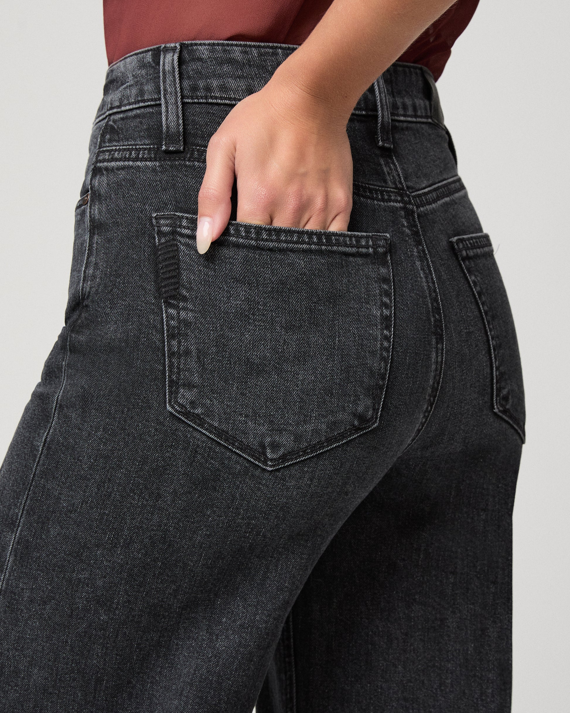 Woman wearing maroon top and black jeans against a white background