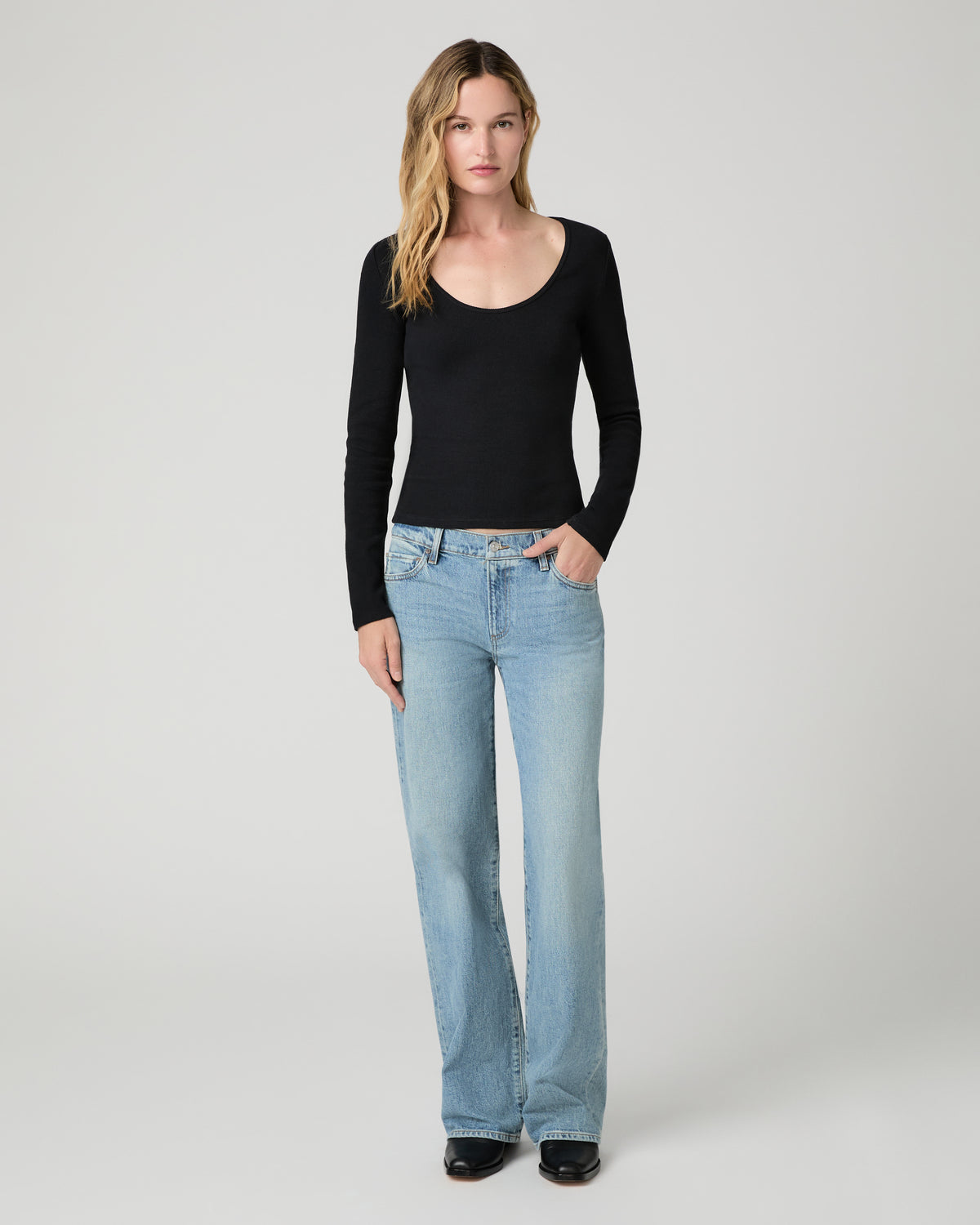 Women wearing a black long sleeve top paired with blue jeans and black boots against a white background
