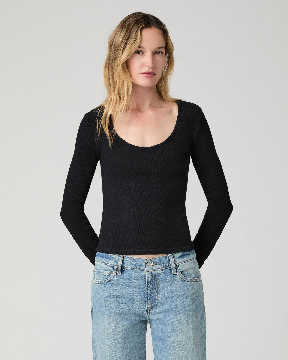 Women wearing a black long sleeve top paired with blue jeans against a white background