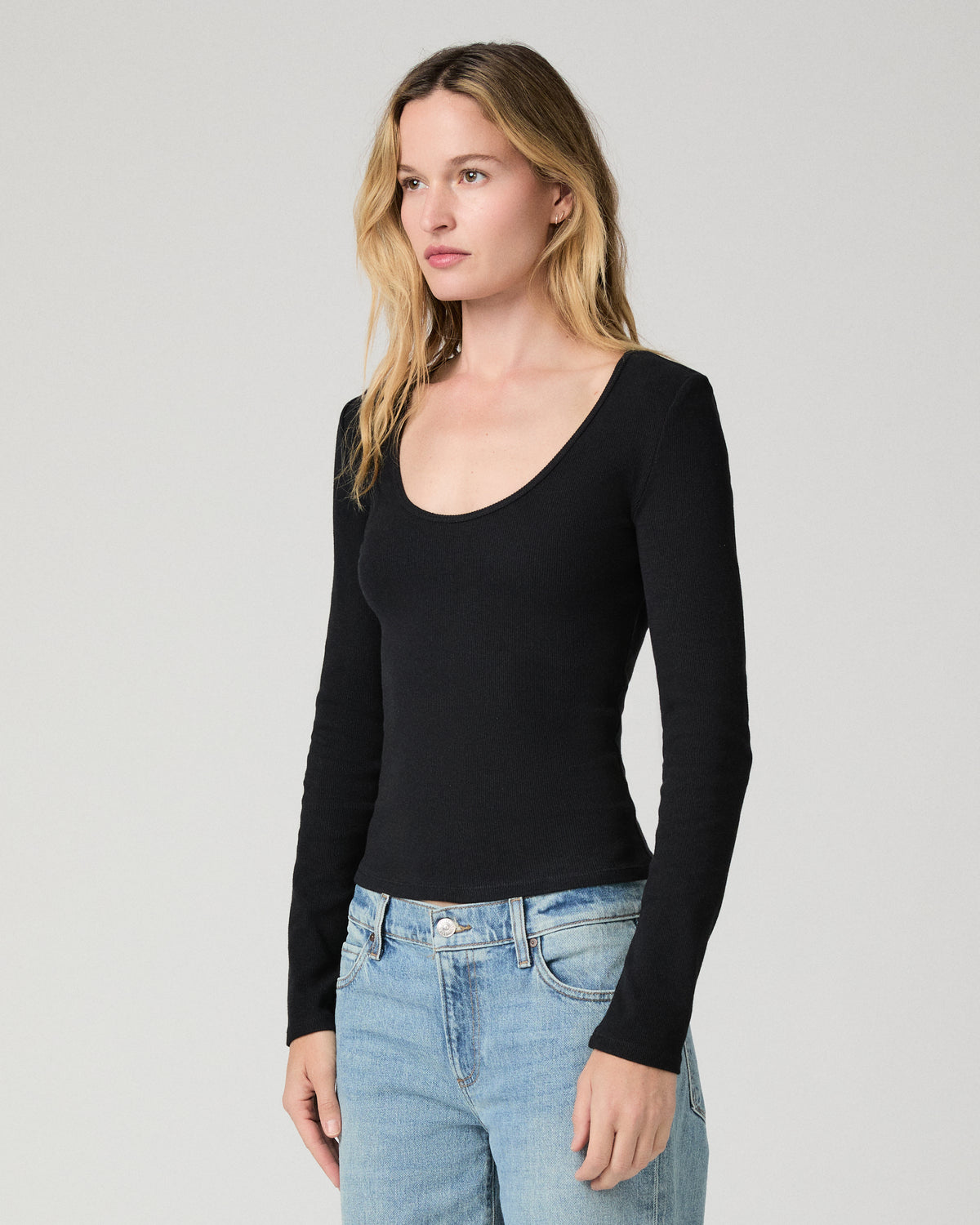 Women wearing a black long sleeve top paired with blue jeans against a white background