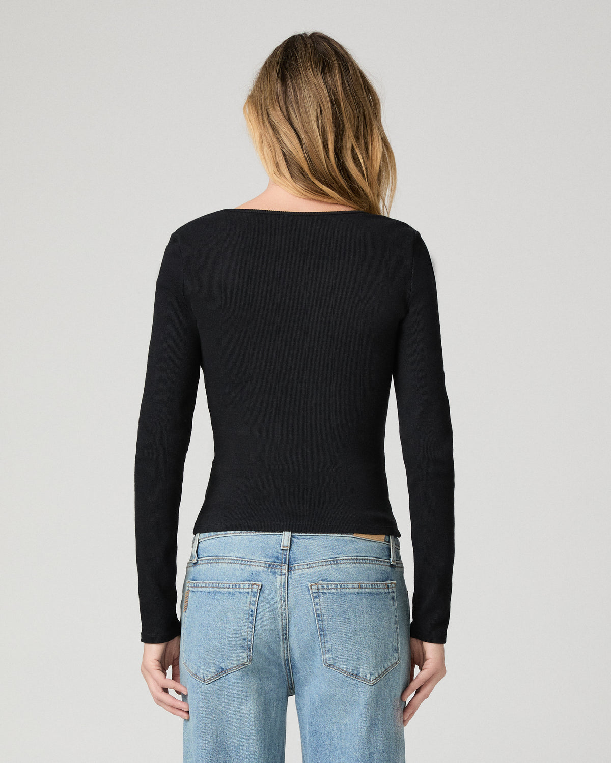 Women wearing a black long sleeve top paired with blue jeans against a white background