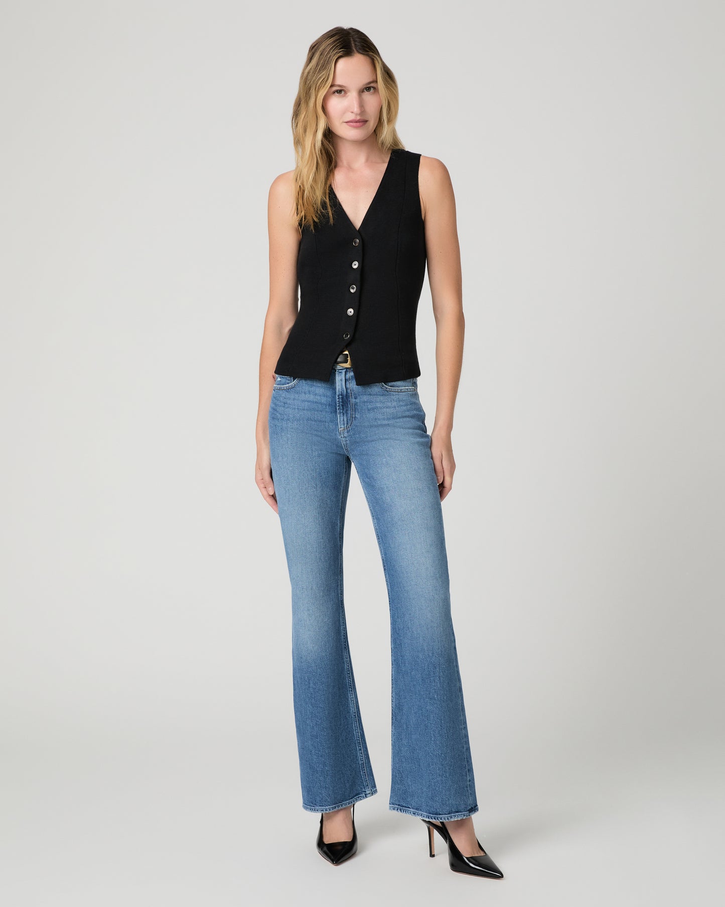 Women wearing a black vest top and blue jeans paired with black heels against a white background