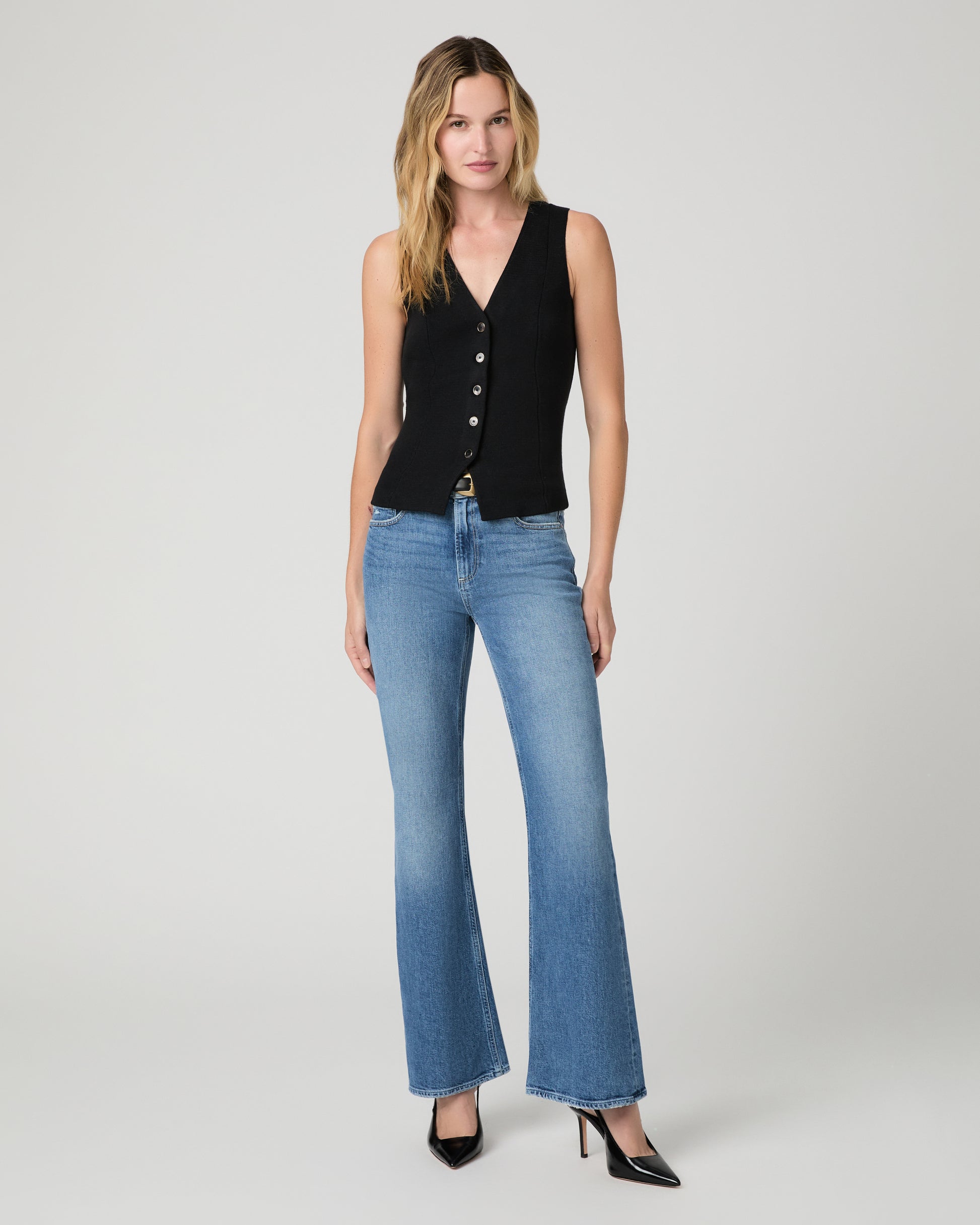 Women wearing a black vest top and blue jeans paired with black heels against a white background