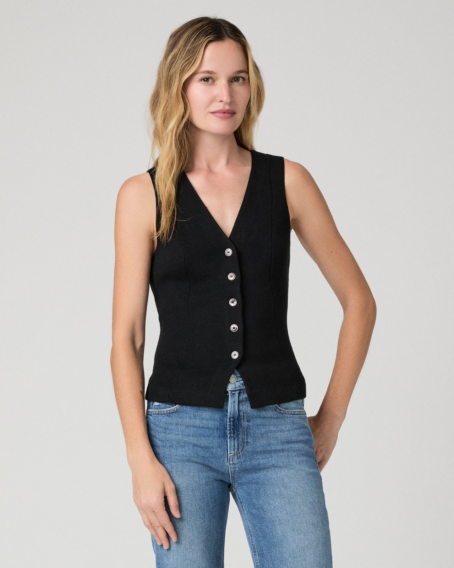 Women wearing a black vest top and blue jeans against a white background
